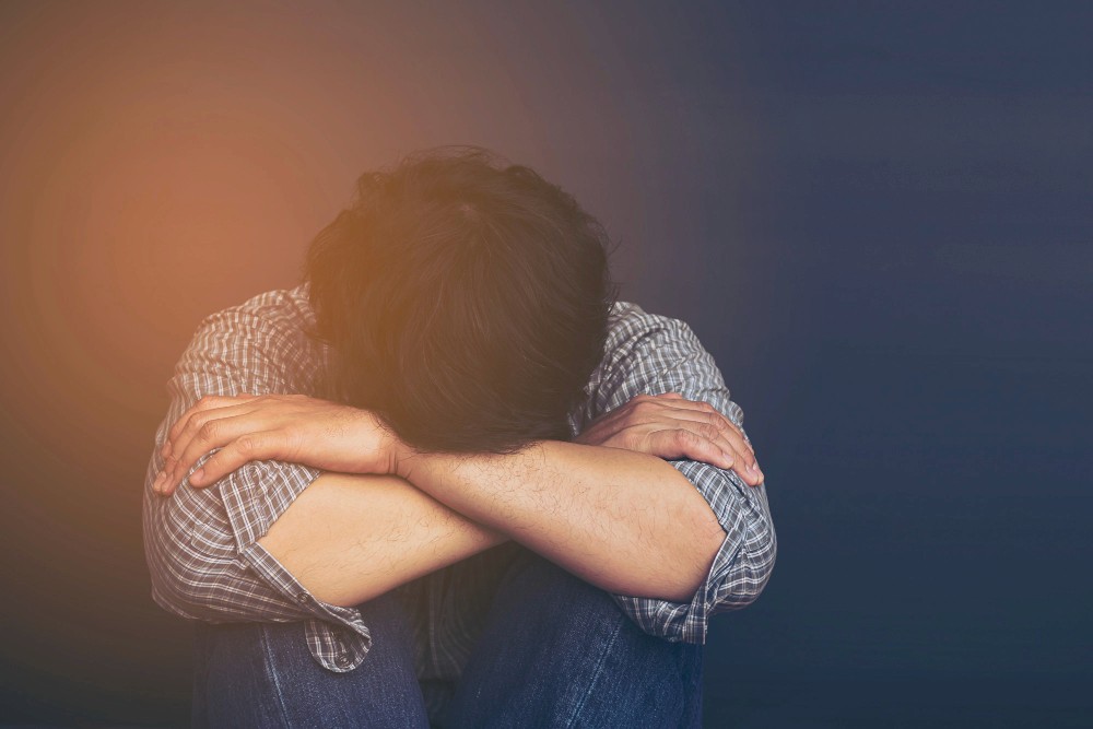 A man sitting on the floor with his arms crossed and head down, depicting sadness and depression.