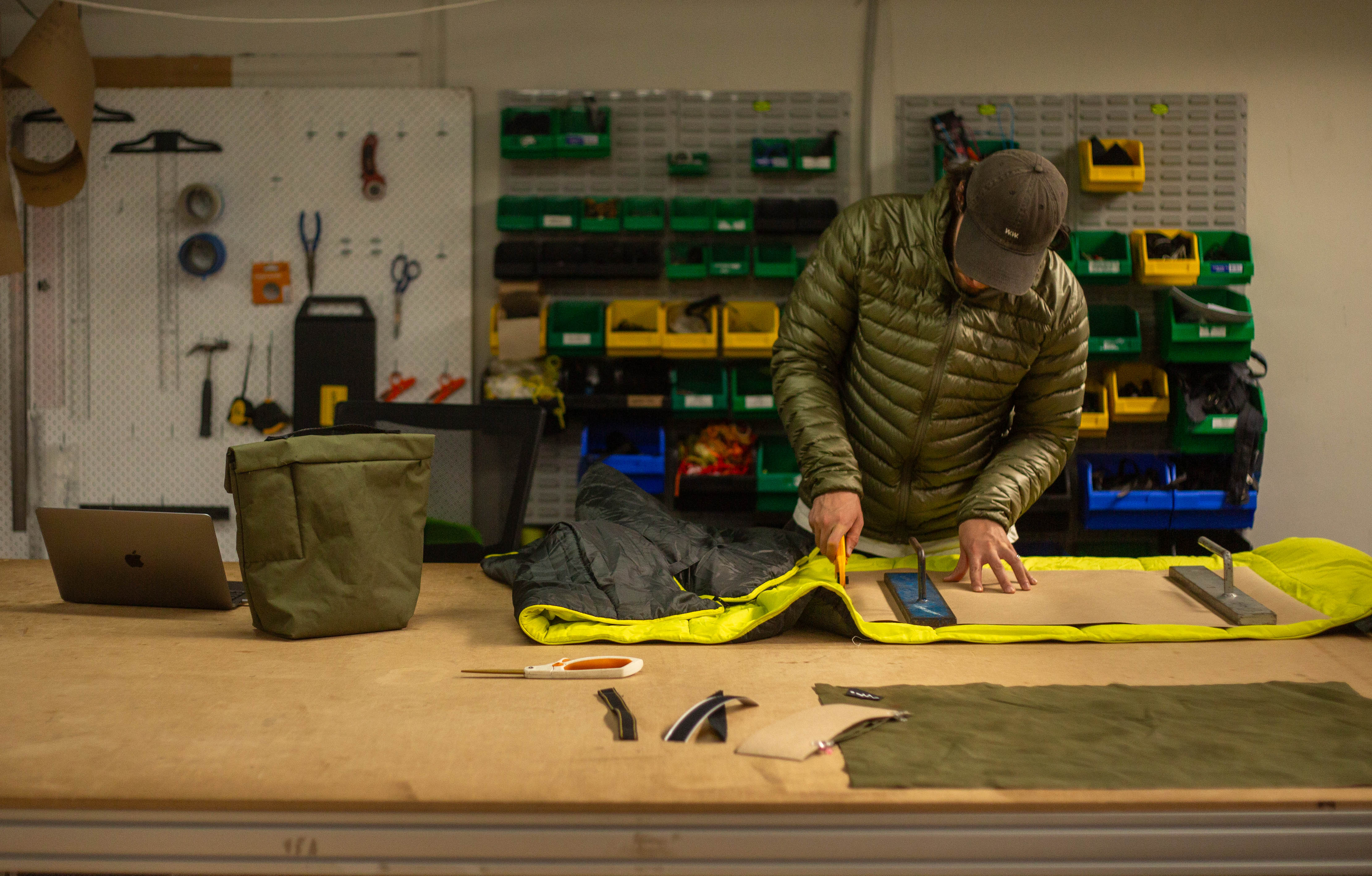 Worker disassembling a synthetic sleeping bag at a factory workbench, preparing materials for technical product development.