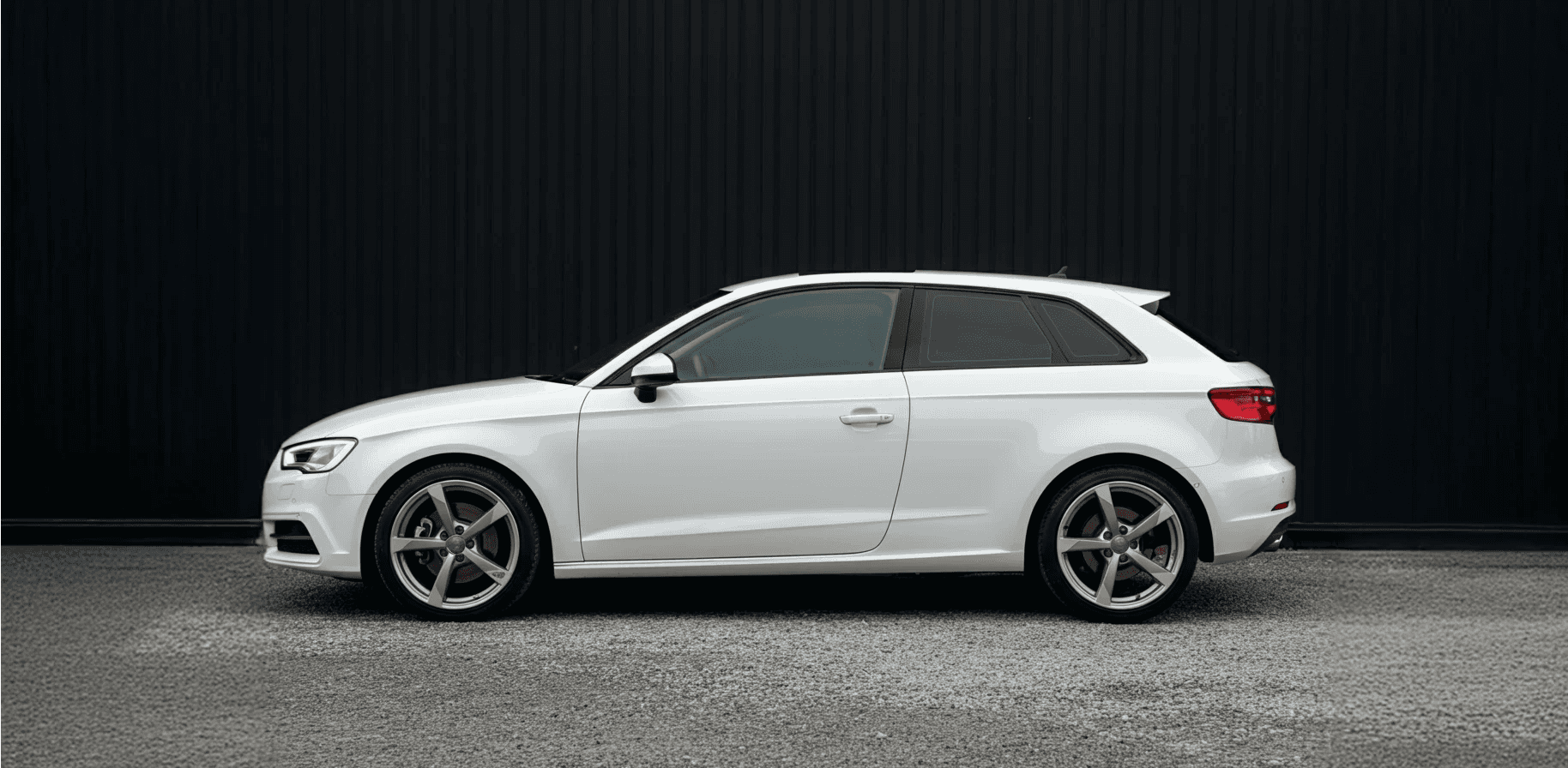 An Audi A3 parked infront of an industrial black building.