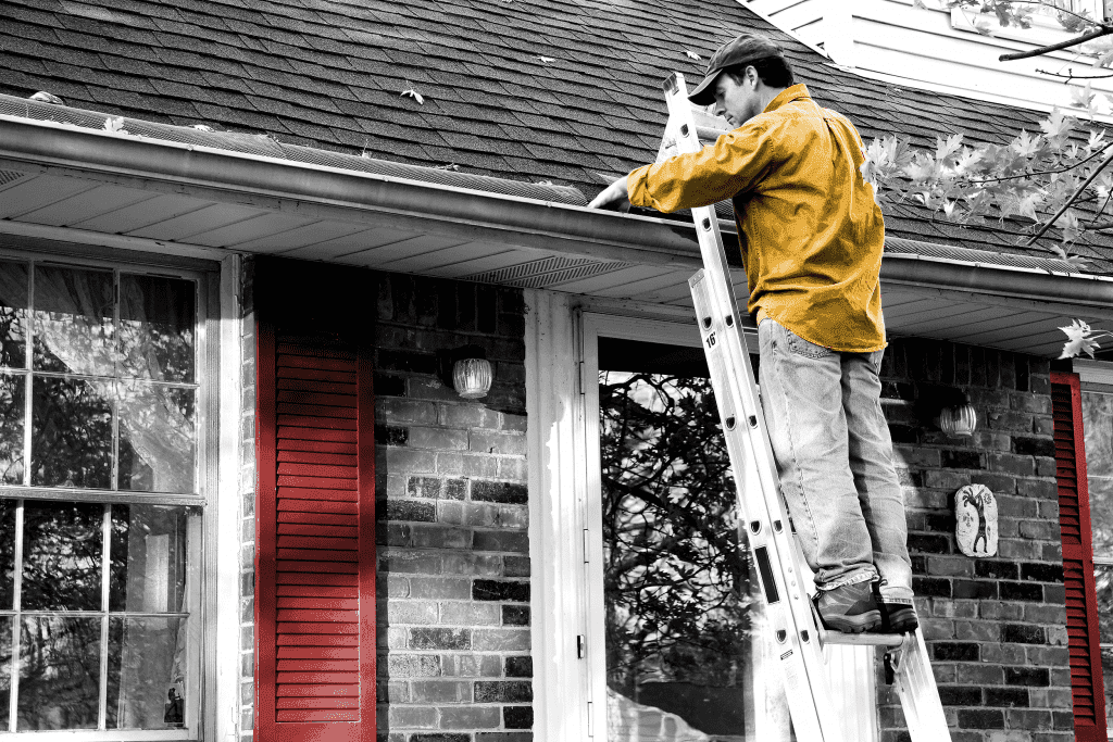 a worker on a ladder cleaning roof of a house