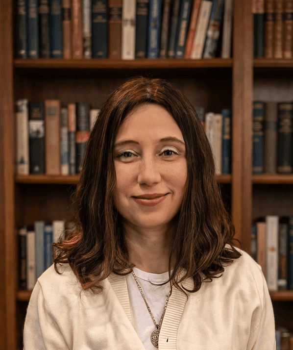 Smiling female therapist with short gray hair, wearing a brown top and a purple shawl, surrounded by a cozy background.