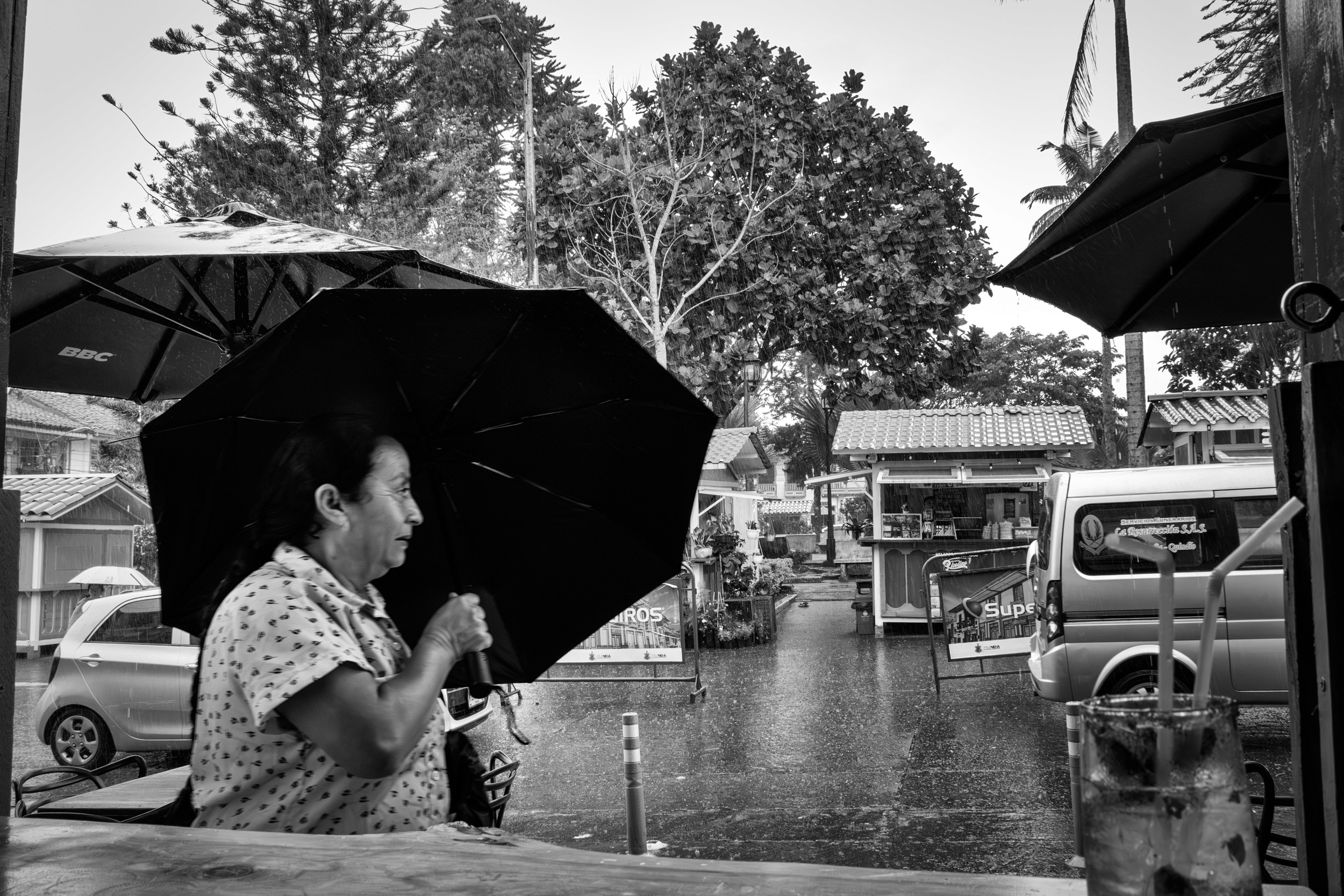 Rainy street scene with people passing by a bar window.