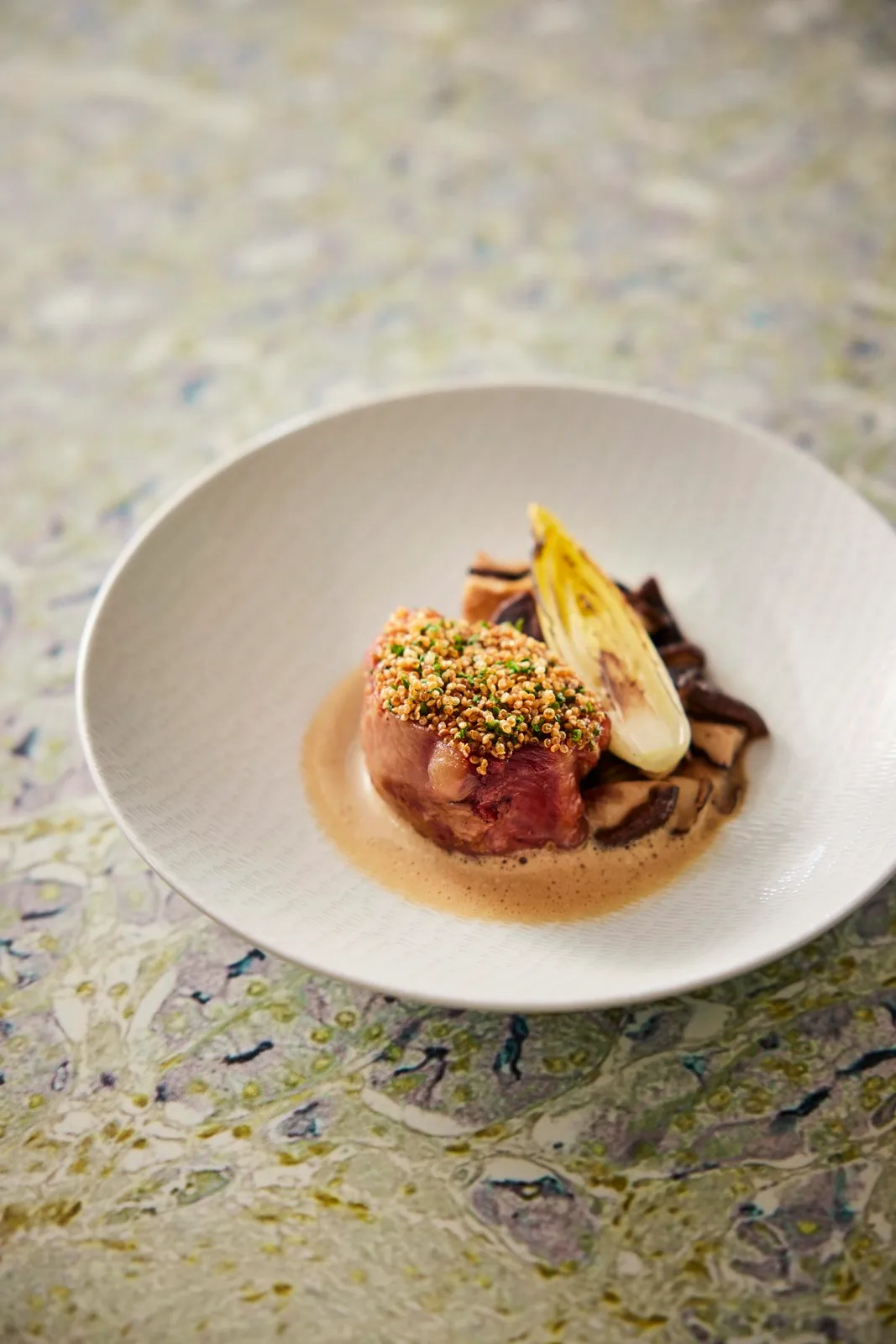 A beautifully plated dish in a white bowl, featuring colorful ingredients on a textured tabletop.