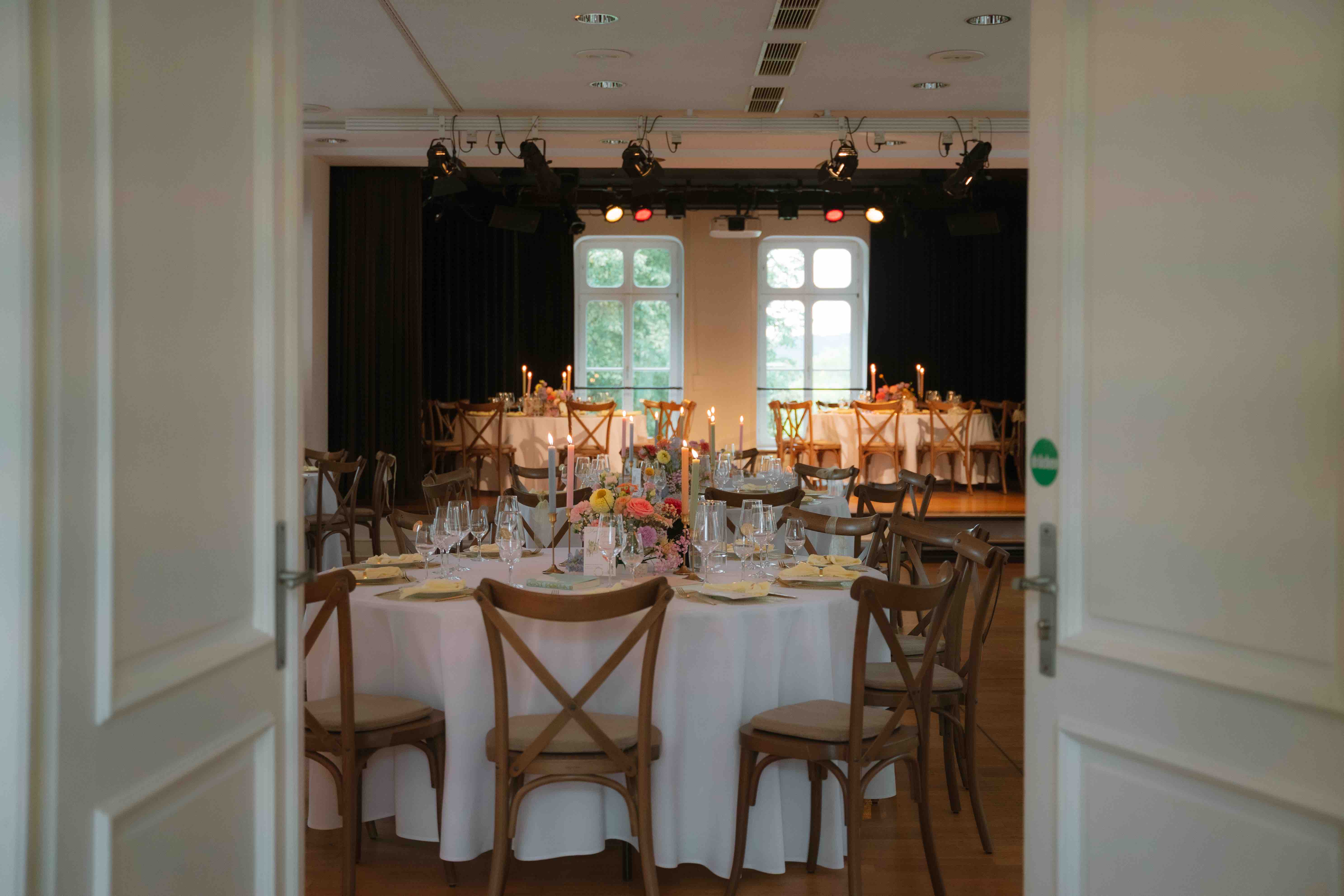 Festlich gedeckte Tische mit Stühlen in einem Raum mit Bühne.