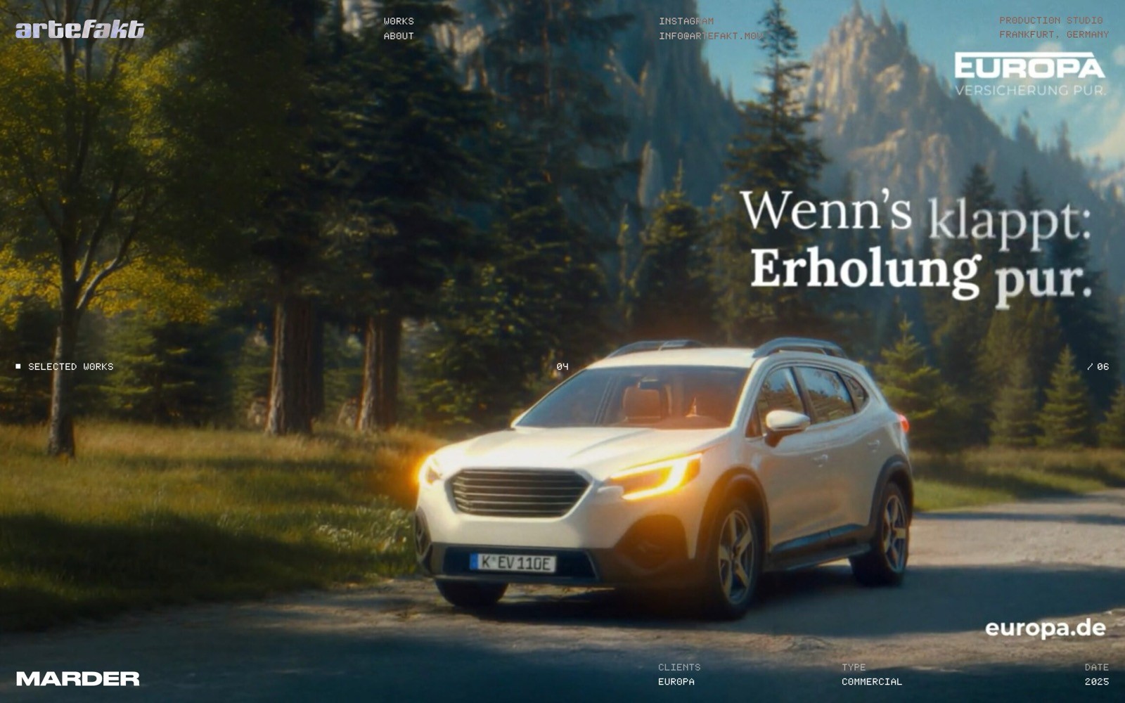 White SUV with headlights on, parked on a dirt road in a forest with mountains in the background.