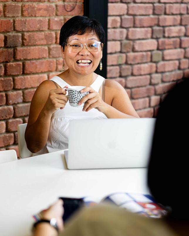 A frontal image of our team member, Mai, holding a cup in her hands and smiling at a person in front of her.