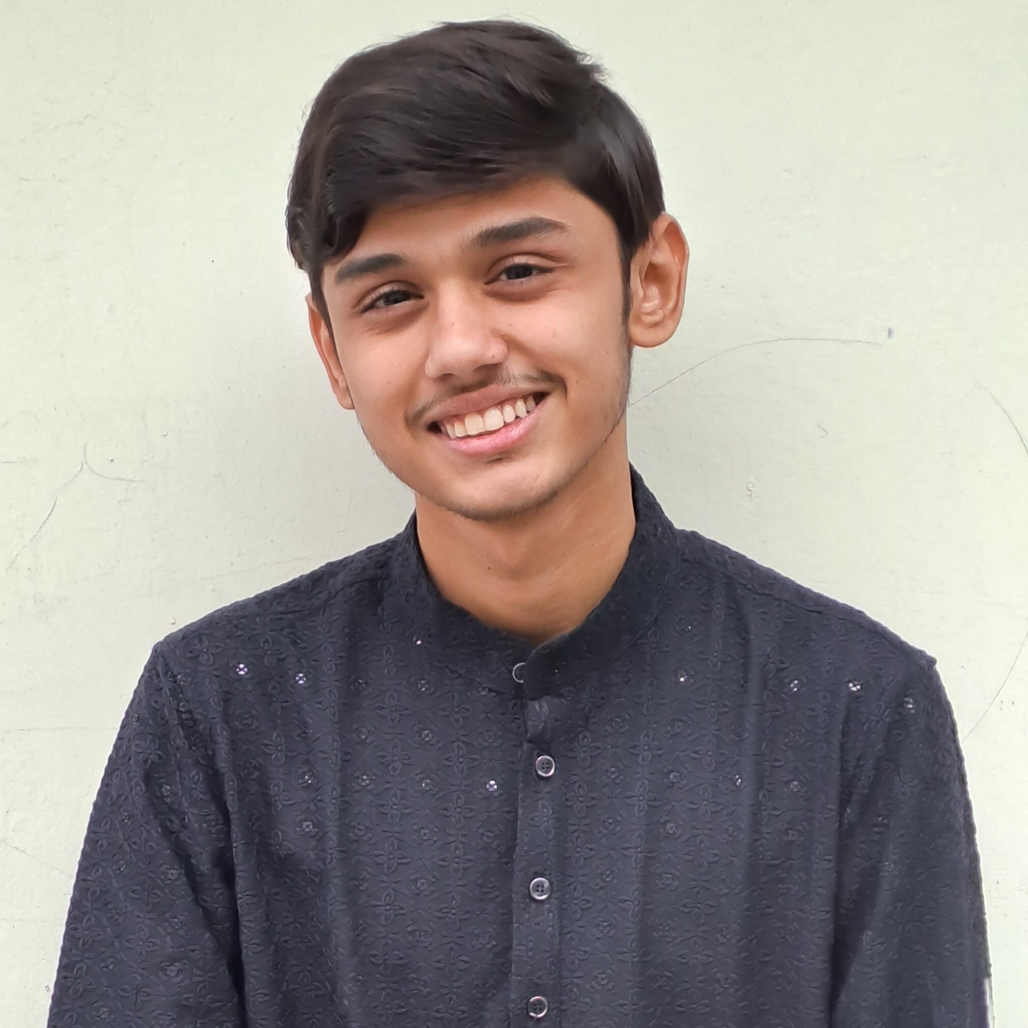 A man with sunglasses and a beard, wearing a green shirt, standing near a beach with palm trees and the ocean in the background.