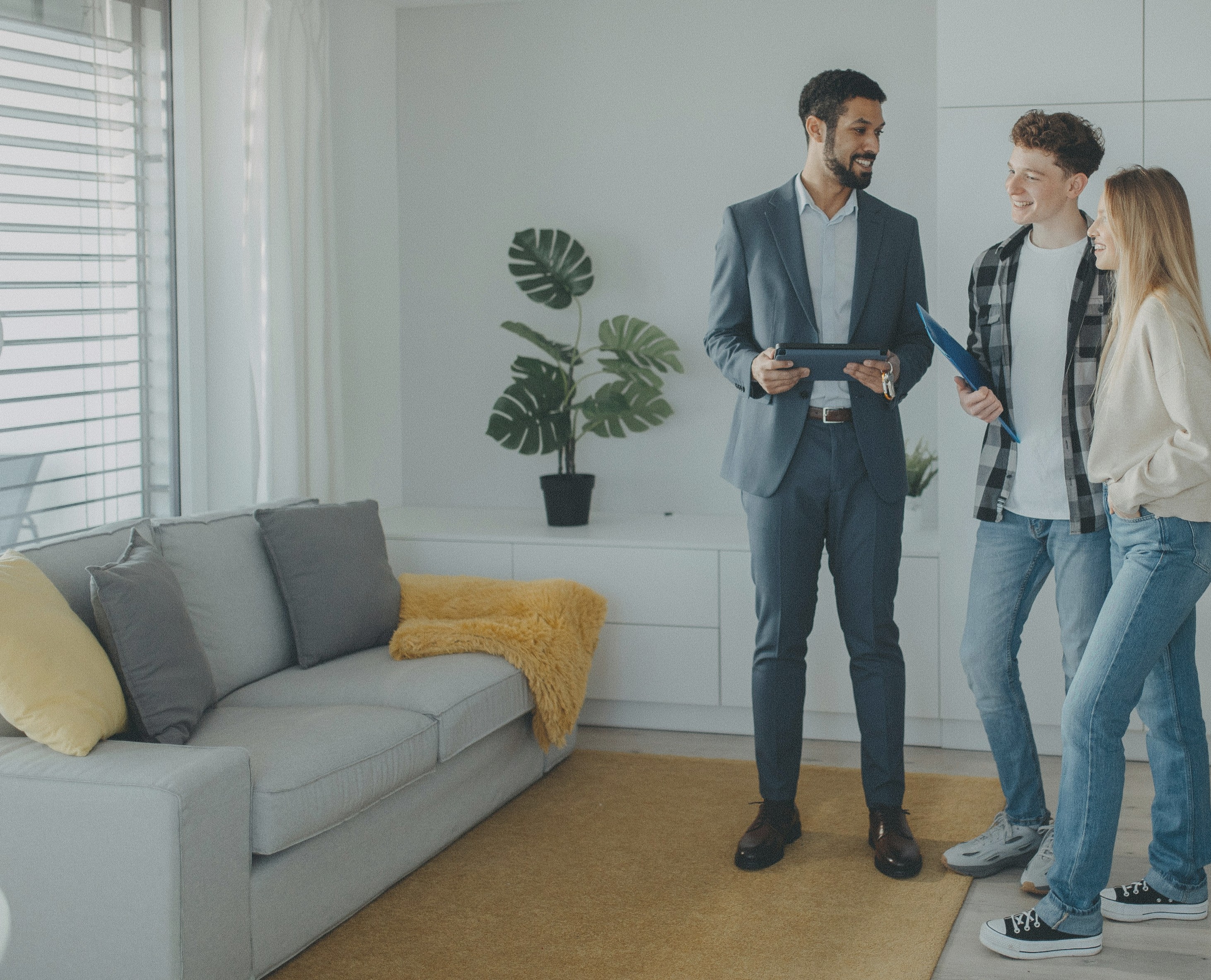 Property agent with a tablet showing a couple around a modern apartment living room