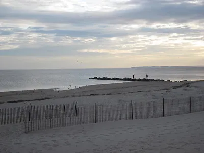 A calm beach scene at dusk with a wooden pier extending into the water under a cloudy sky. This is the bluff by Kings Park.