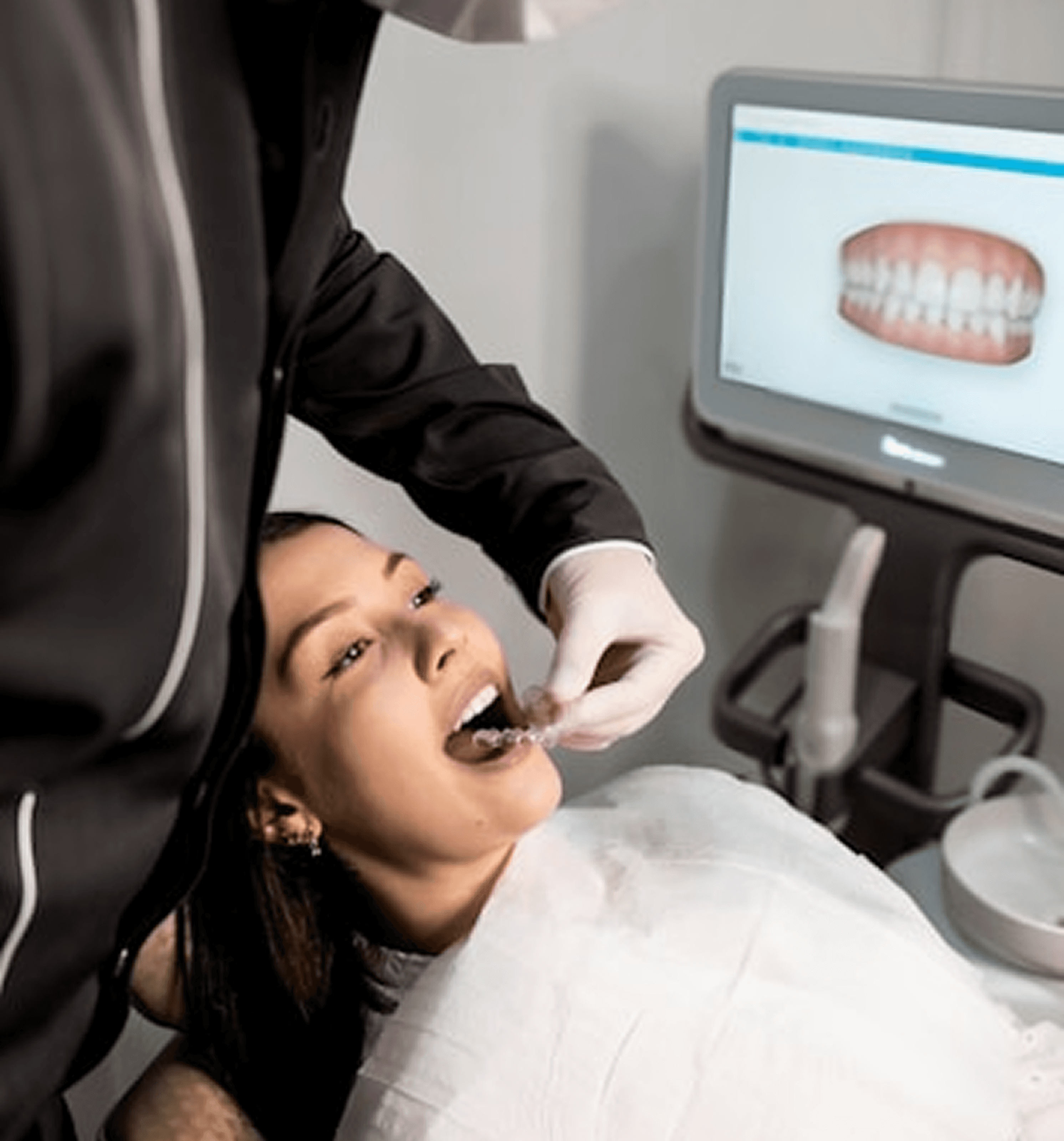 Dental professional placing clear aligner in patient’s mouth with digital teeth image on monitor