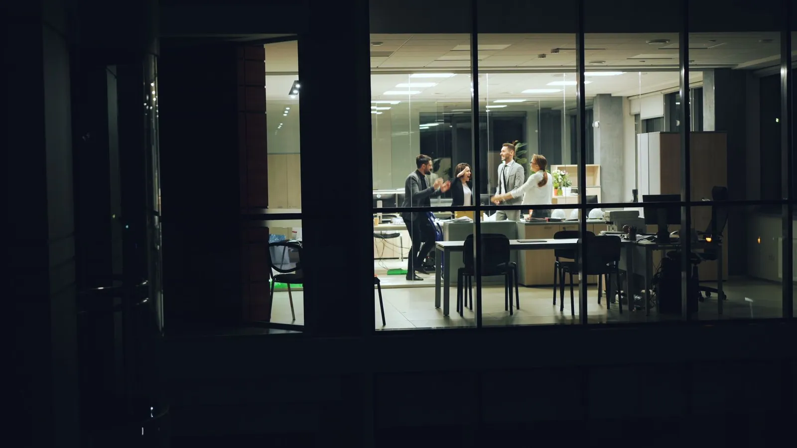 A lit glass-walled office floor at night, seen from outside