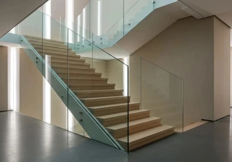 Modern wooden staircase with clear glass railings in a well-lit residential interior for safety compliance.