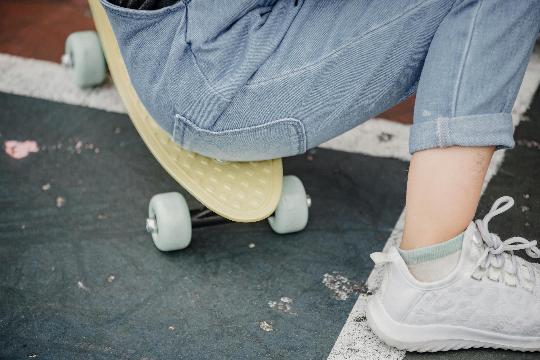 Crop anonymous child in jeans and sneakers sitting on penny board while having break from riding