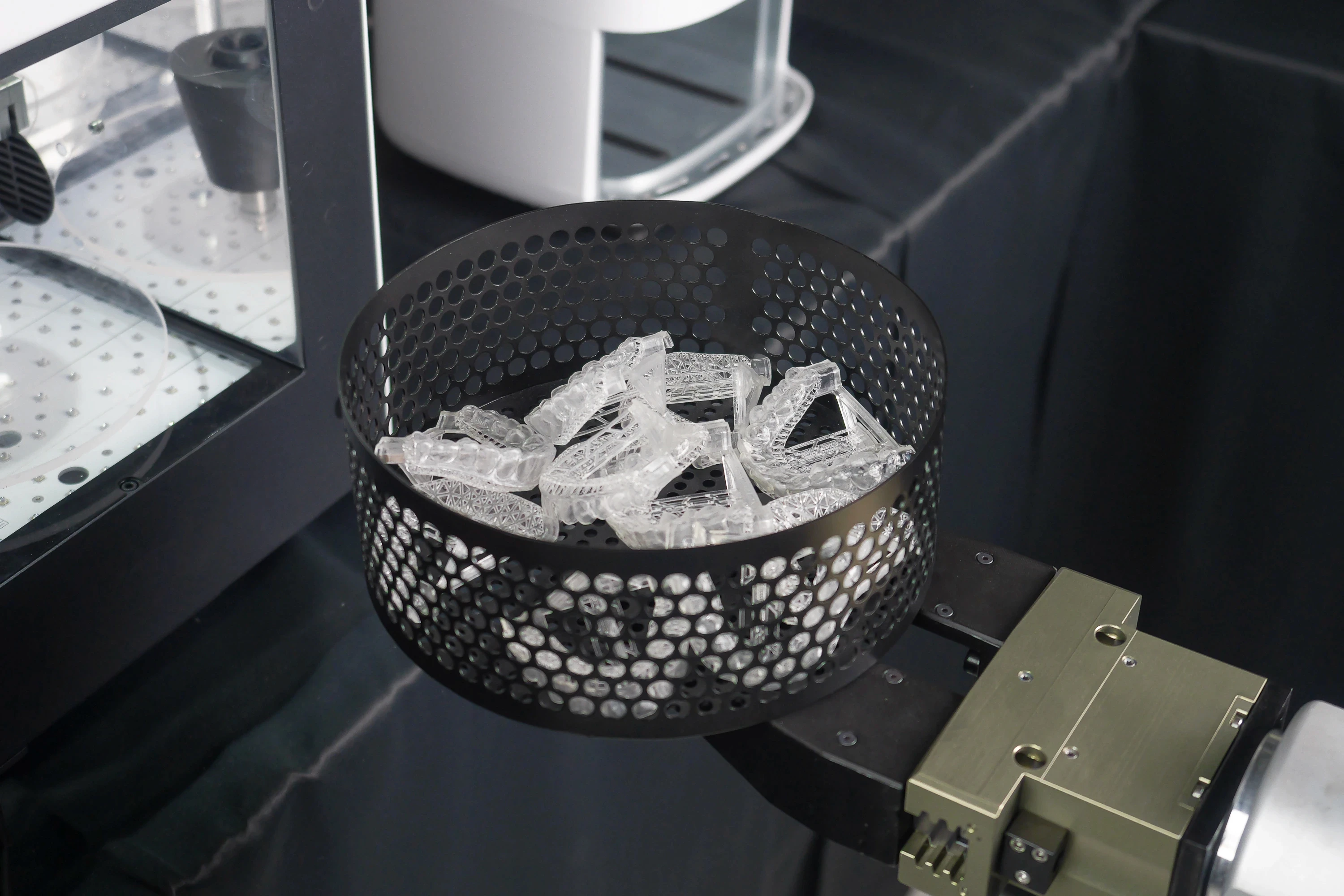 Close-up of 3D printed clear aligners inside a perforated automation basket ready for the curing cycle.