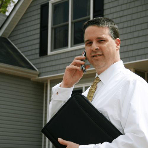 Portrait of a woman with pulled-back hair, wearing a textured sweater, seated in warm natural light against a soft brown background.
