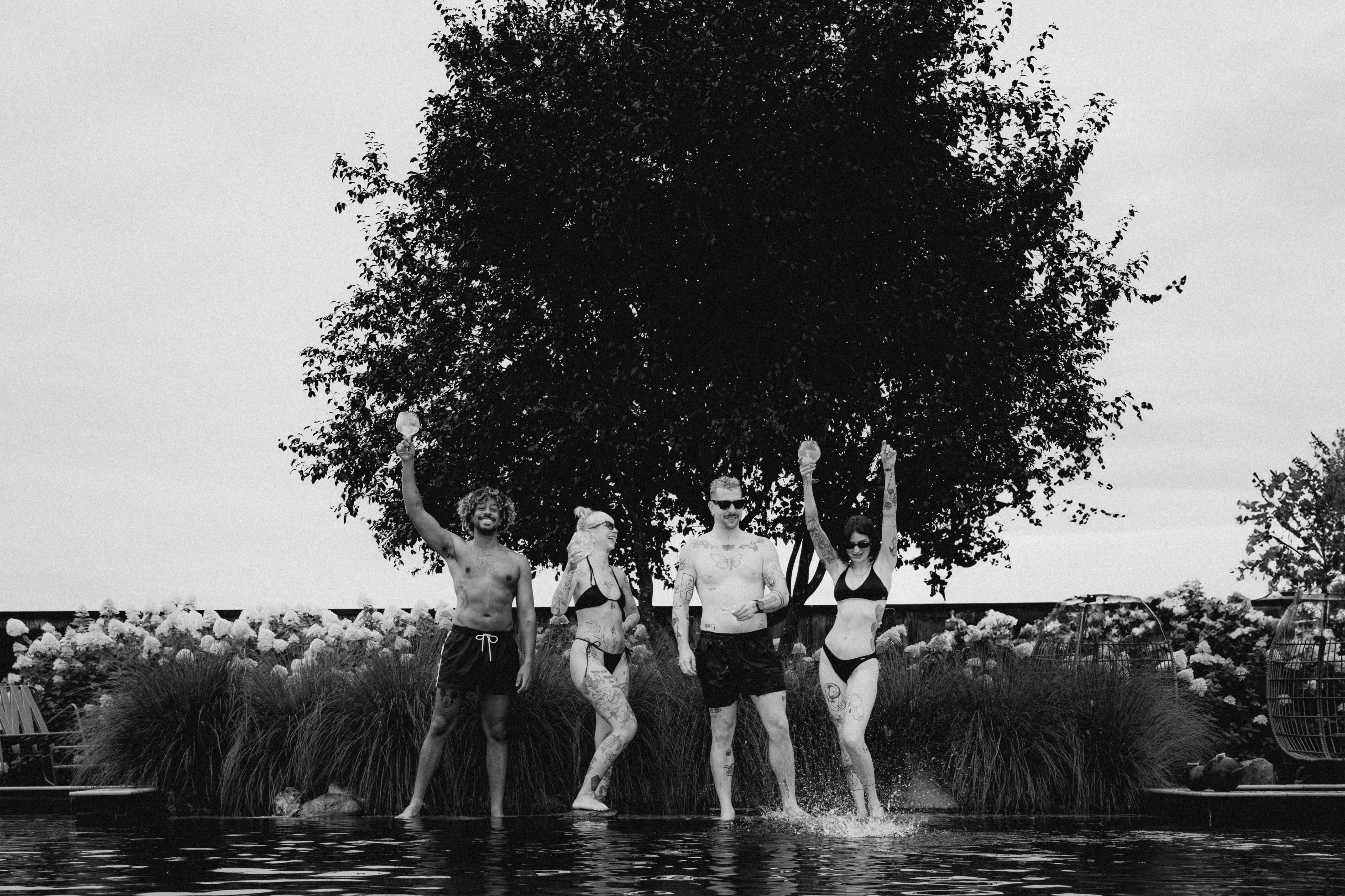Two figures stand near a large tree in a serene landscape, captured in black and white.