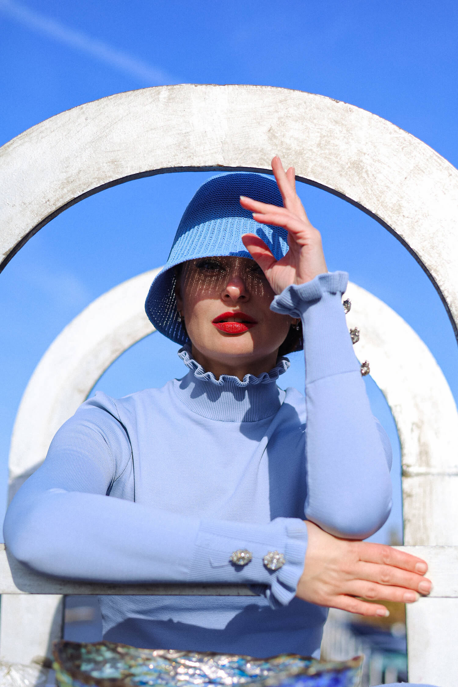Close-up editorial portrait with blue styling, red lipstick and dramatic sunlight shadows.