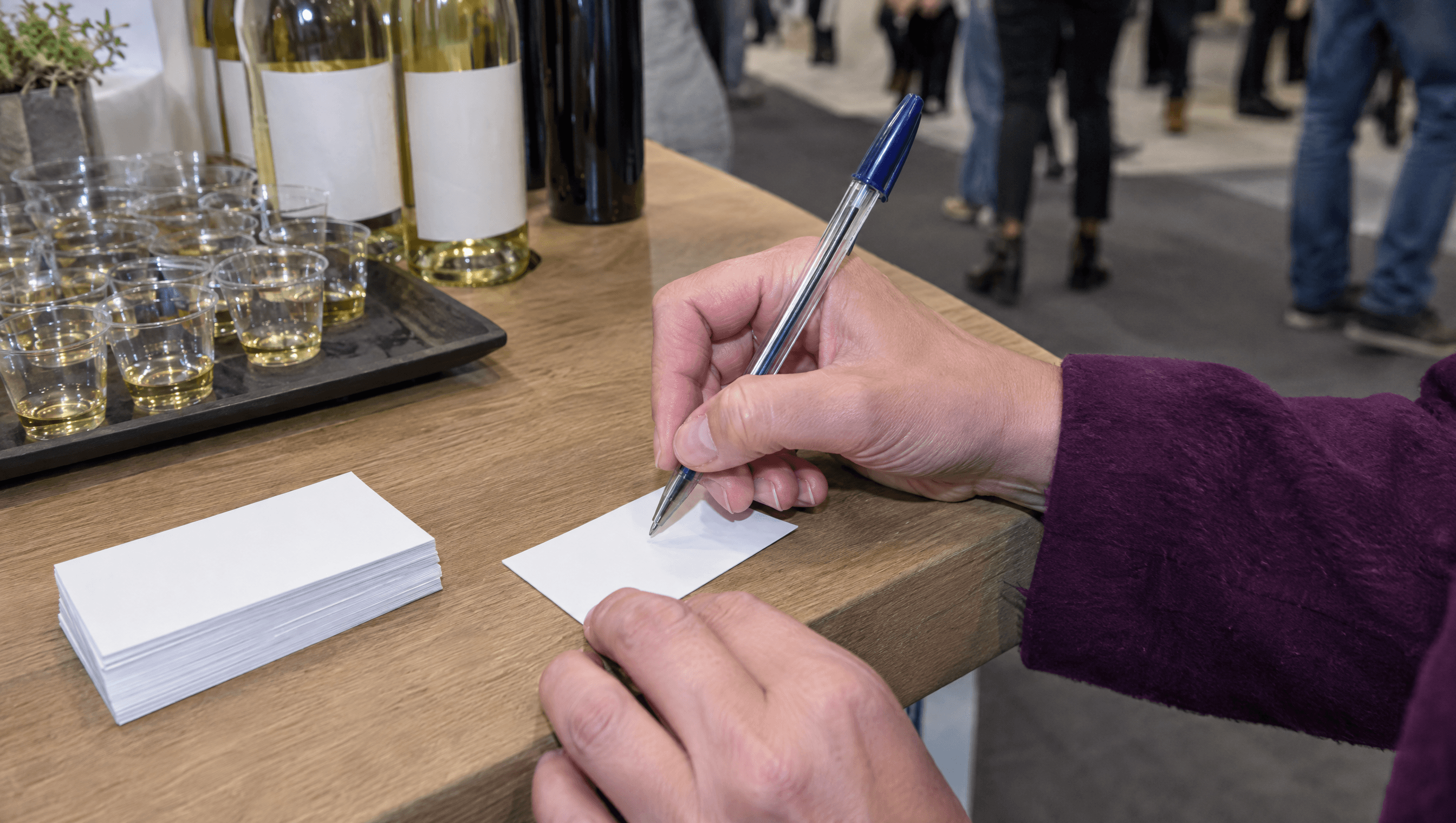 Een standhouder schrijft een notitie op de achterkant van een visitekaartje, naast een dienblad met proefglaasjes