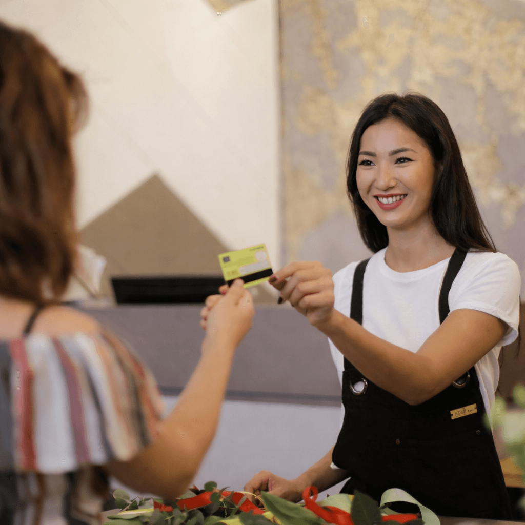Smiling cashier processes payment in a small business focused on communications, using AI-enhanced business phone systems for customer engagement.