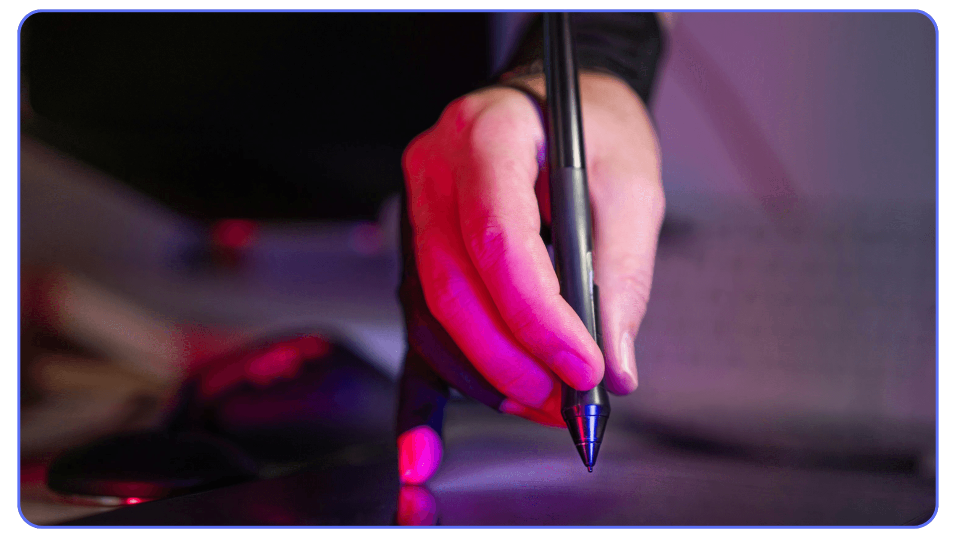 Close-up of a person using a stylus pen on a digital tablet under purple lighting, representing digital drawing or design work.