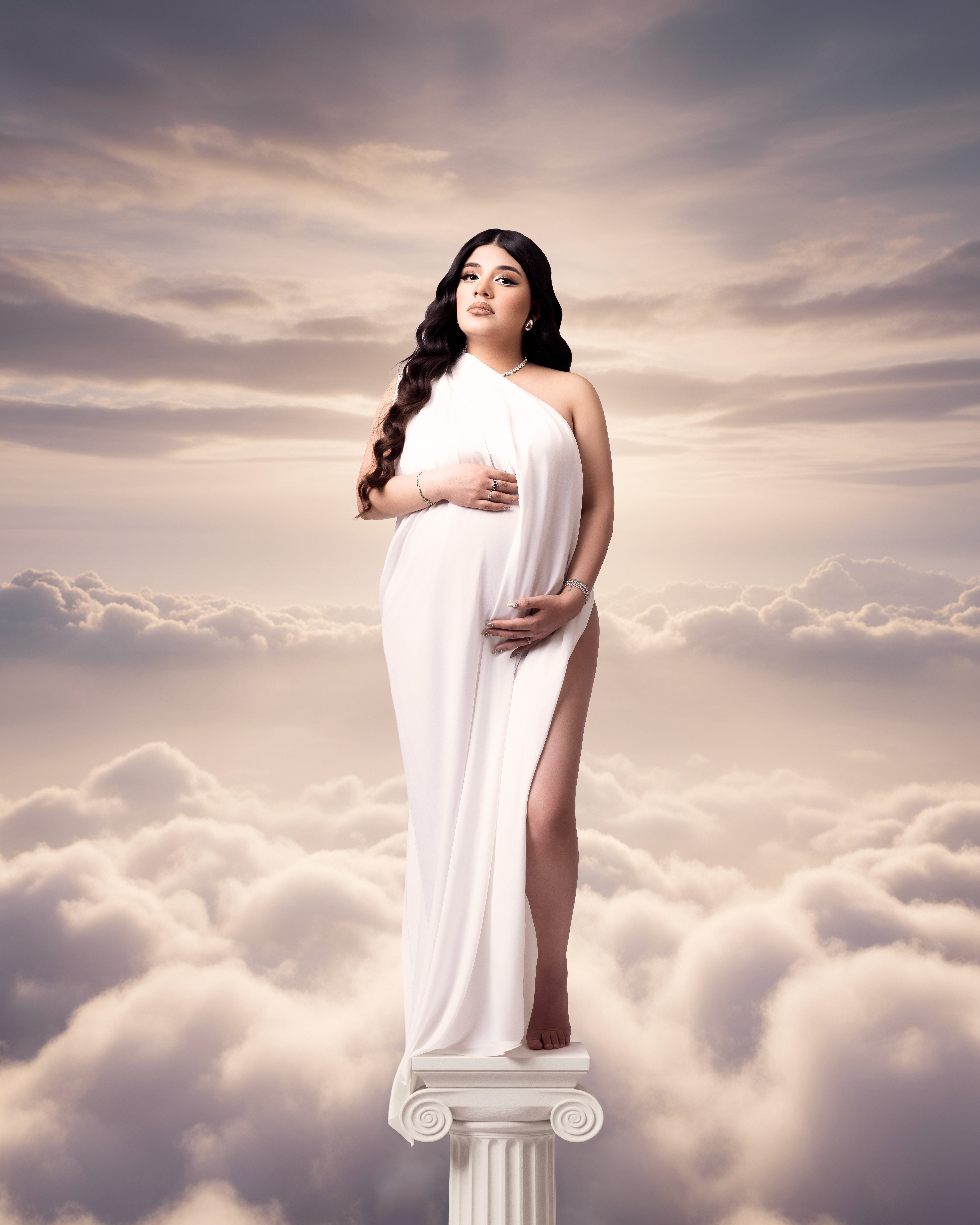 mamá embarazada posando con tela blanca y columnas griegas y fondo digital de nubes