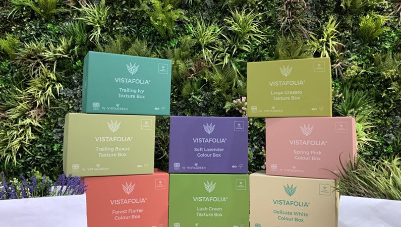 Colorful stacked VistaFolia texture boxes containing various styles of artificial plants such as Trailing Ivy, Large Grasses, Soft Lavender, Delicate White, and Forest Flame.