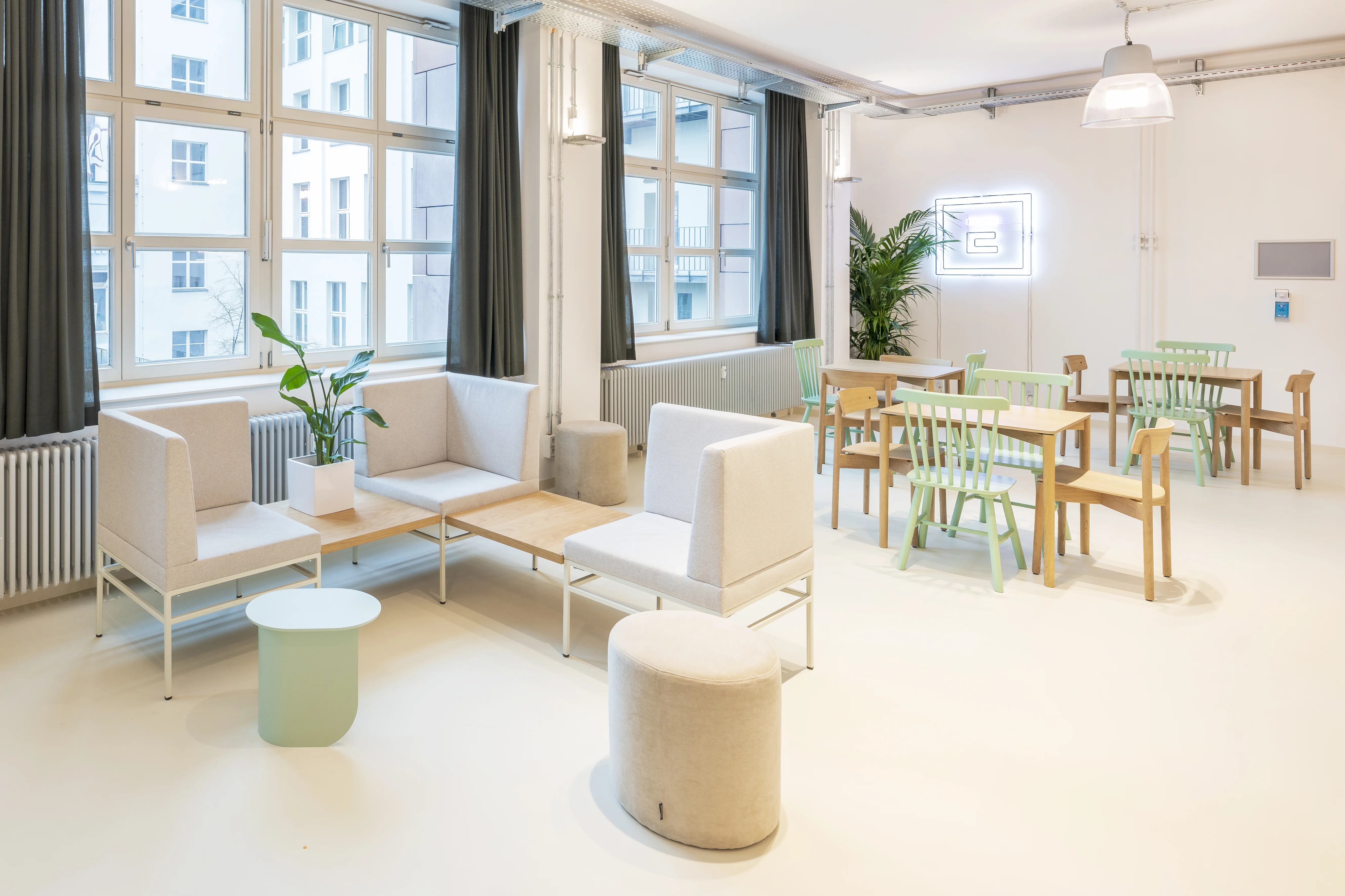 Lounge and dining area at ELEMENT with beige high-back sofas, a mint side table, beige poufs, wooden tables with mint and natural chairs, a neon logo on the wall and grey curtains.