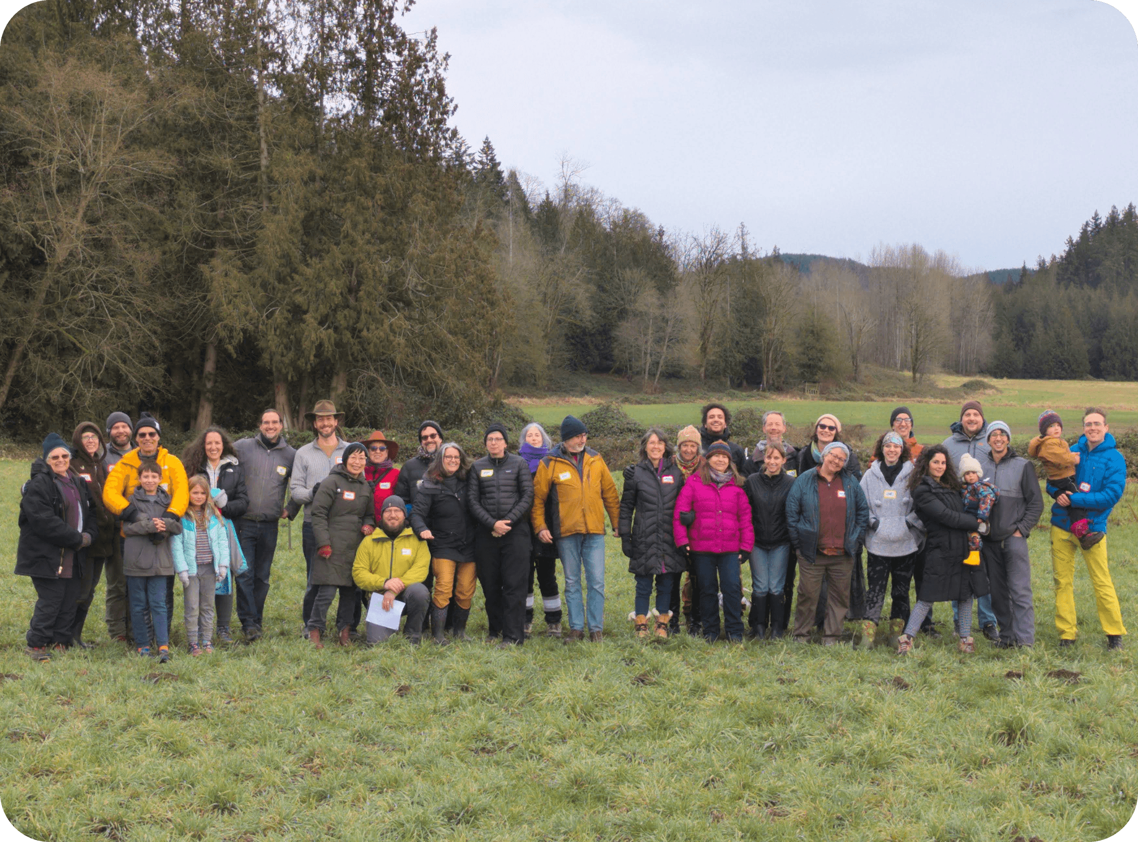 A small group of people walking together along a hiking trail through the land at Rooted Northwest, surrounded by forest and open space.