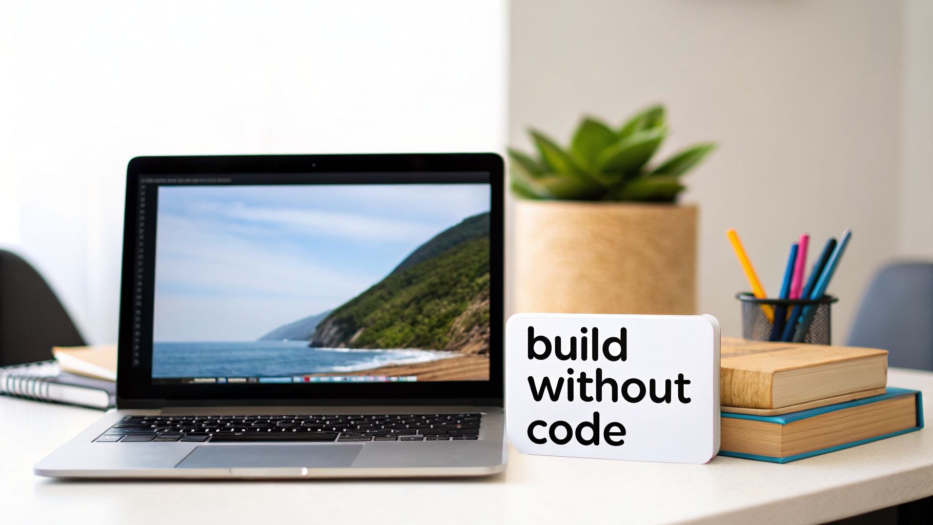 A clean workspace featuring a laptop, a 'build without code' sign, a plant, and books.