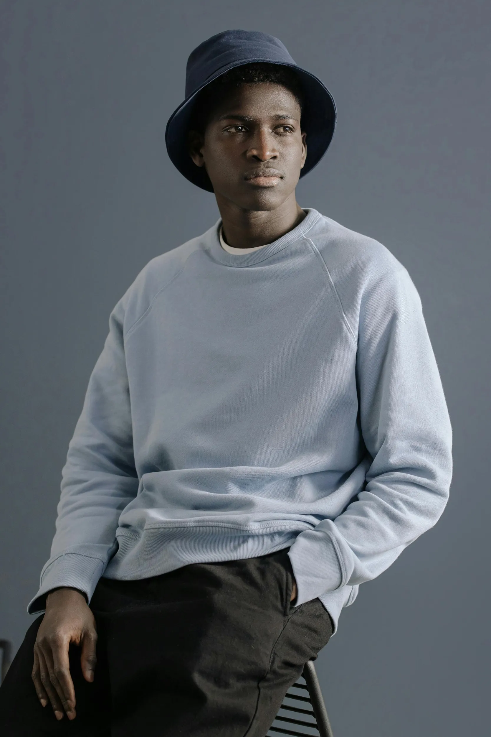 Male model wearing minimalist sweatshirt and bucket hat in studio, contemporary fashion portrait