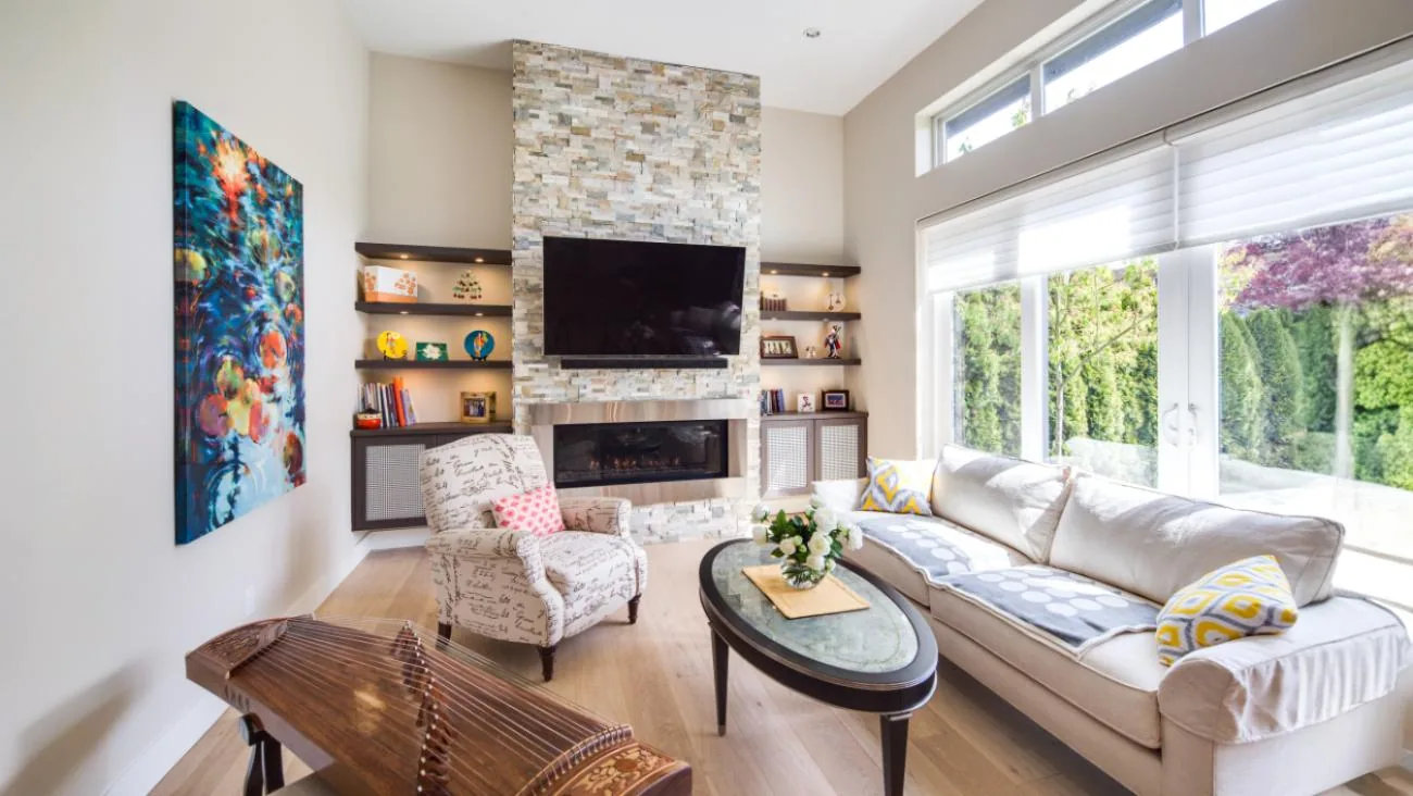 Spacious family room with two-story ceiling, natural stone fireplace, floating wood shelves, large windows, and open floor plan in custom Vancouver home