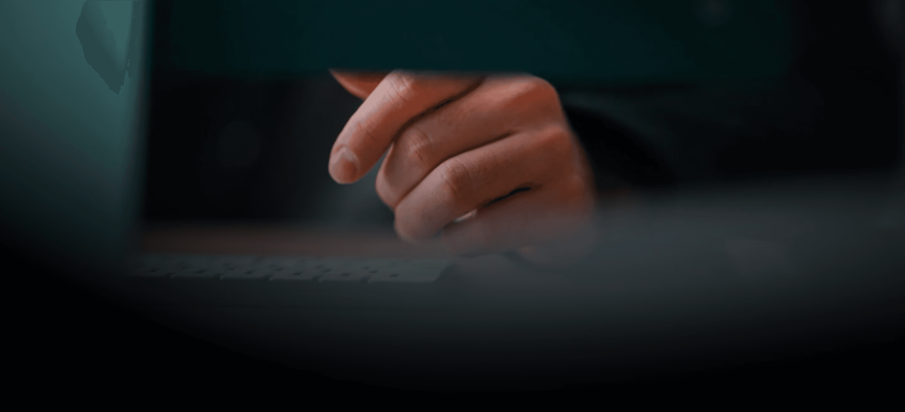 A person's hand with warm, natural skin tones hovers above a dark keyboard, illuminated by a soft cool blue light from a.