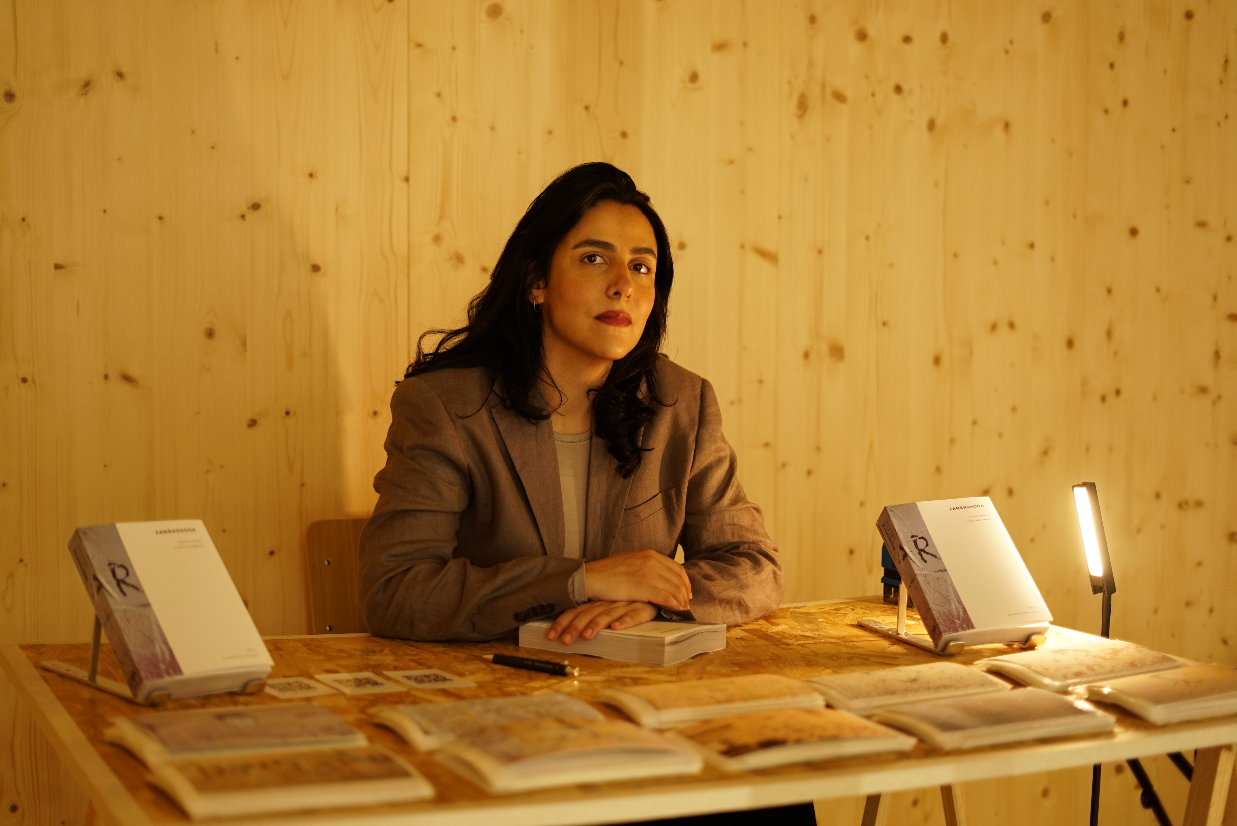 Photographie de l'autrice Parand Danesh entourée de son roman Zamânshoor et de ses tirages