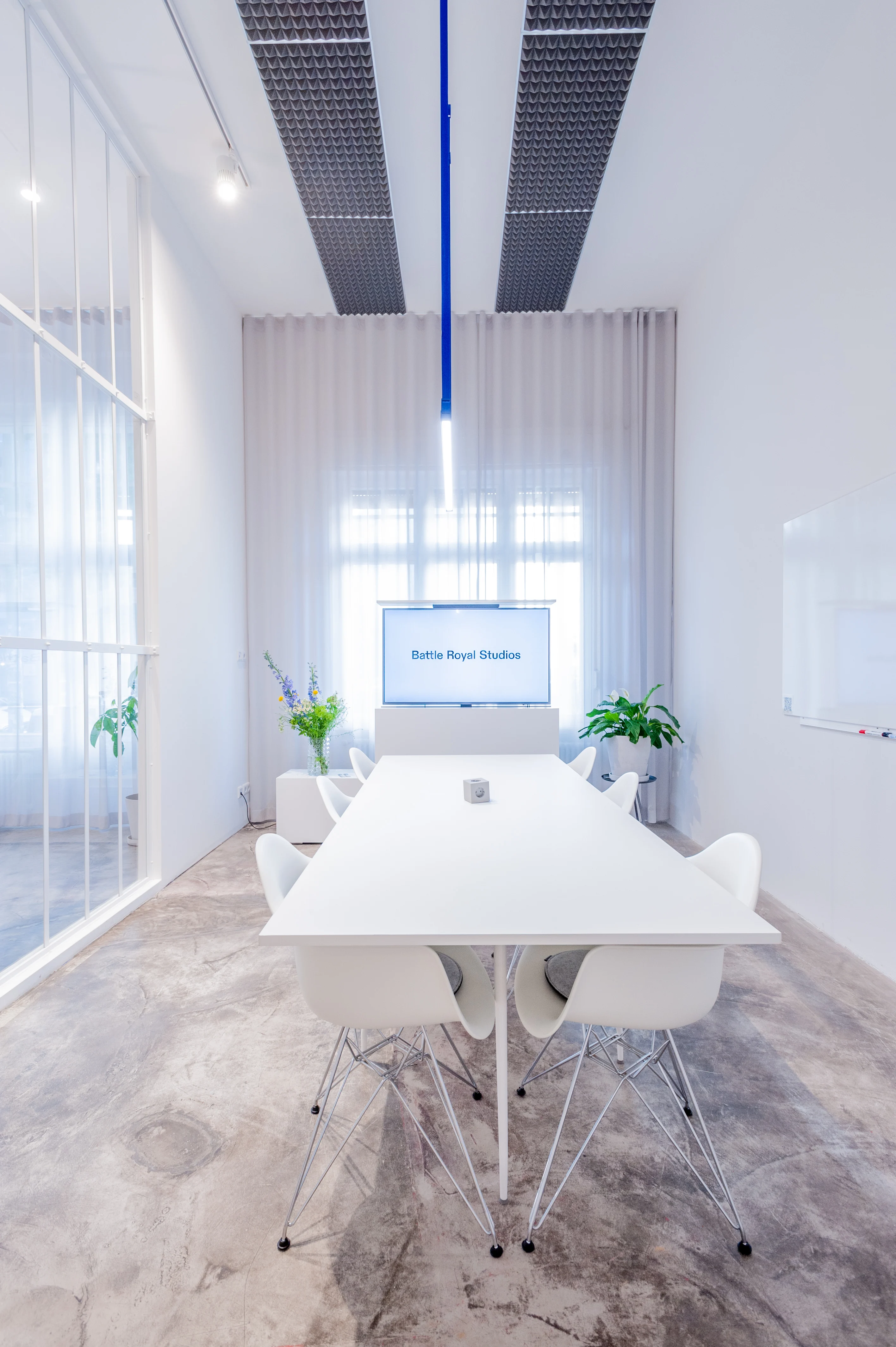 Conference room at BATTLE ROYAL with white table and wire-base shell chairs, a presentation screen, black grid acoustic ceiling, a vertical cobalt-blue pendant light and a whiteboard on the wall.