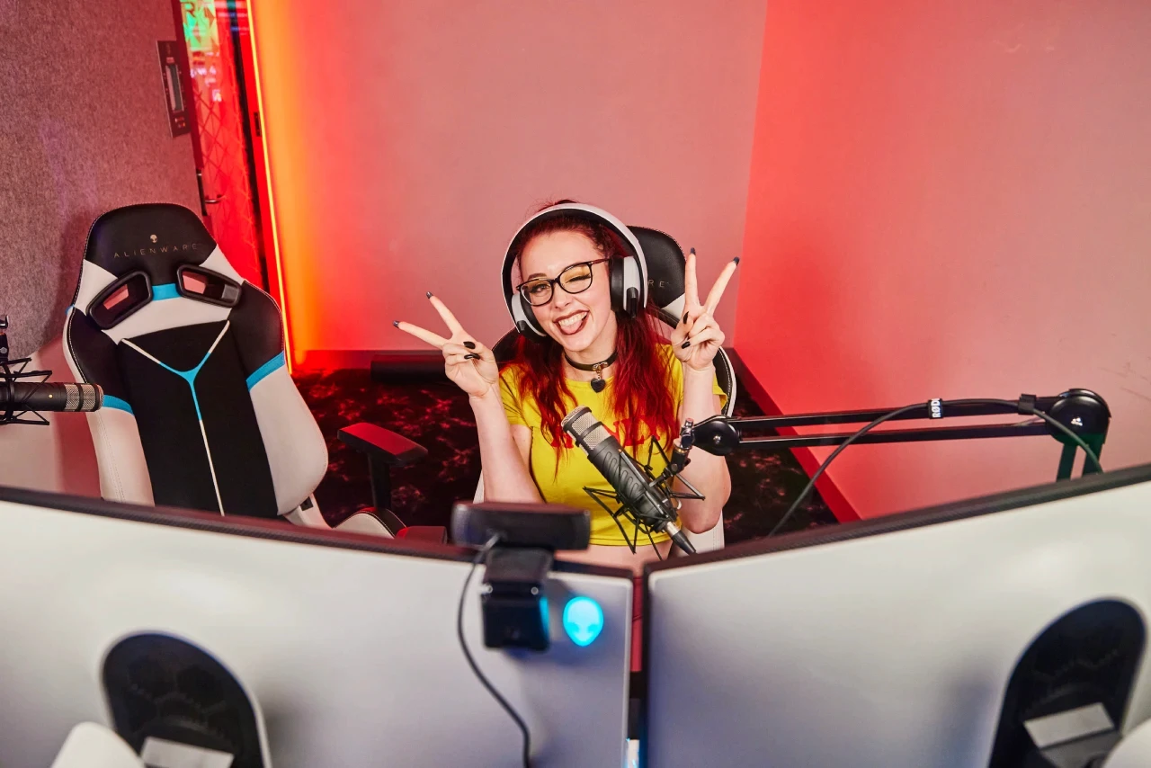 A person holding up their hands to make a peace sign sitting in front of a computer in the Streamer Pod at Fortress