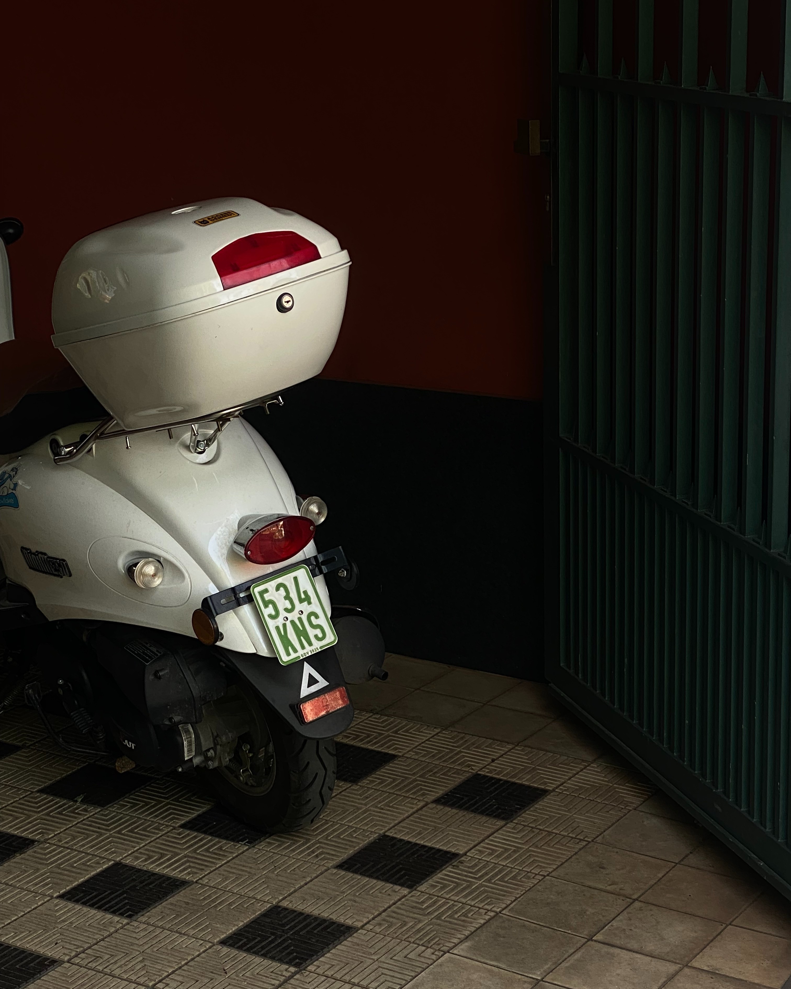 A picture of a moped parked in a gate in Berlin with red, green, light beige and black colors.