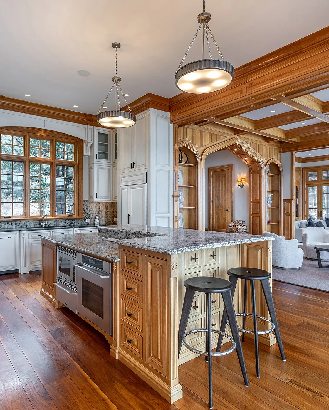 Modern kitchen with a large island, wooden cabinetry, bar stools, and large windows letting in natural light.