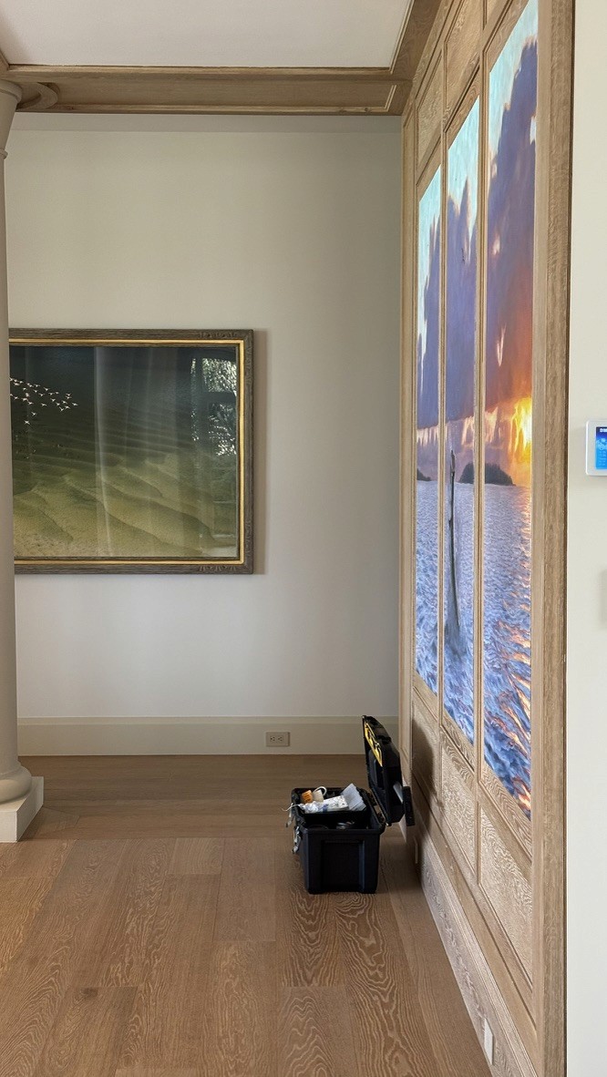 Framed bird flock photograph beside a wood-paneled wall inset with a sunset seascape triptych