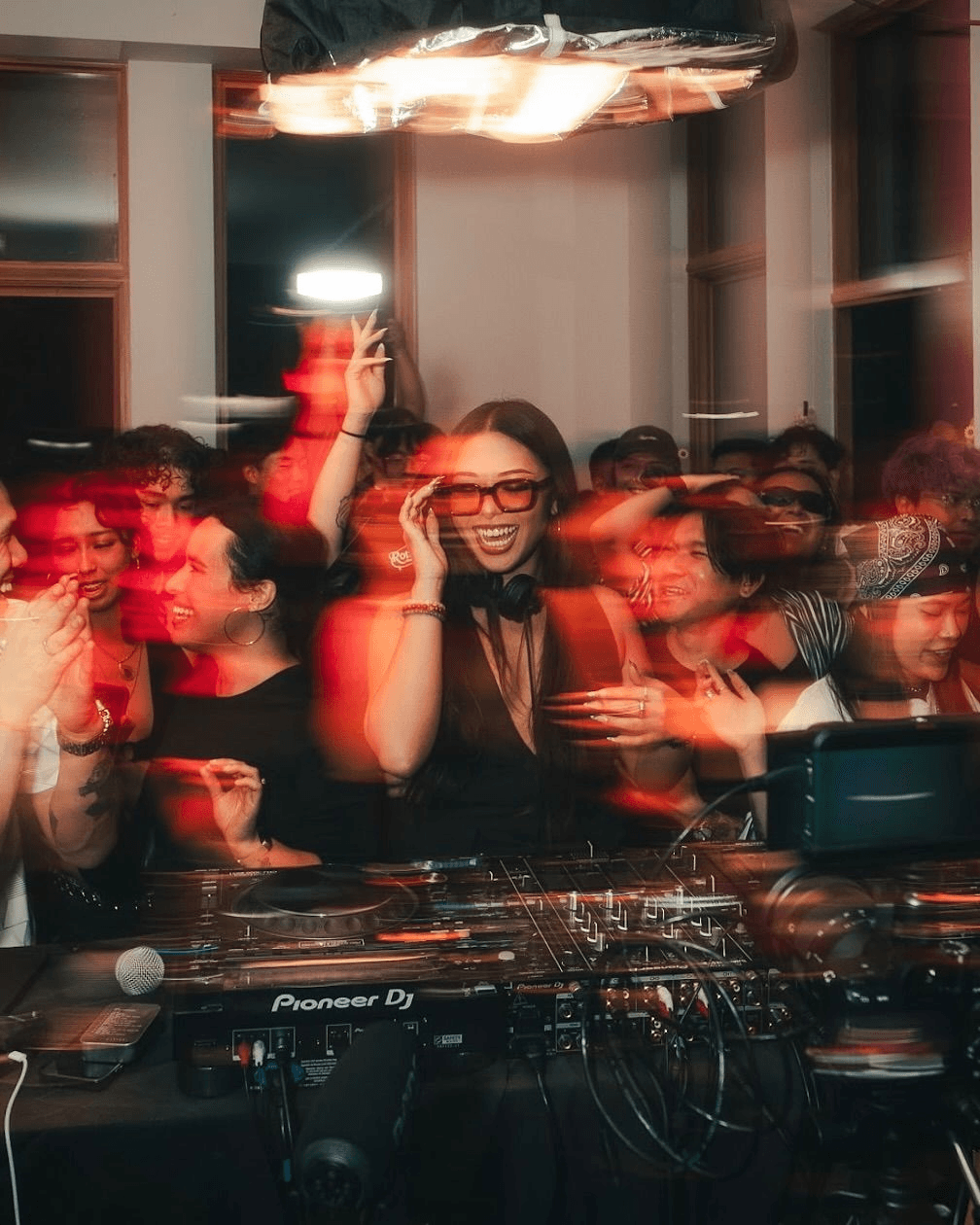 Long-exposure event photo of a smiling DJ surrounded by a dancing crowd at a nightclub