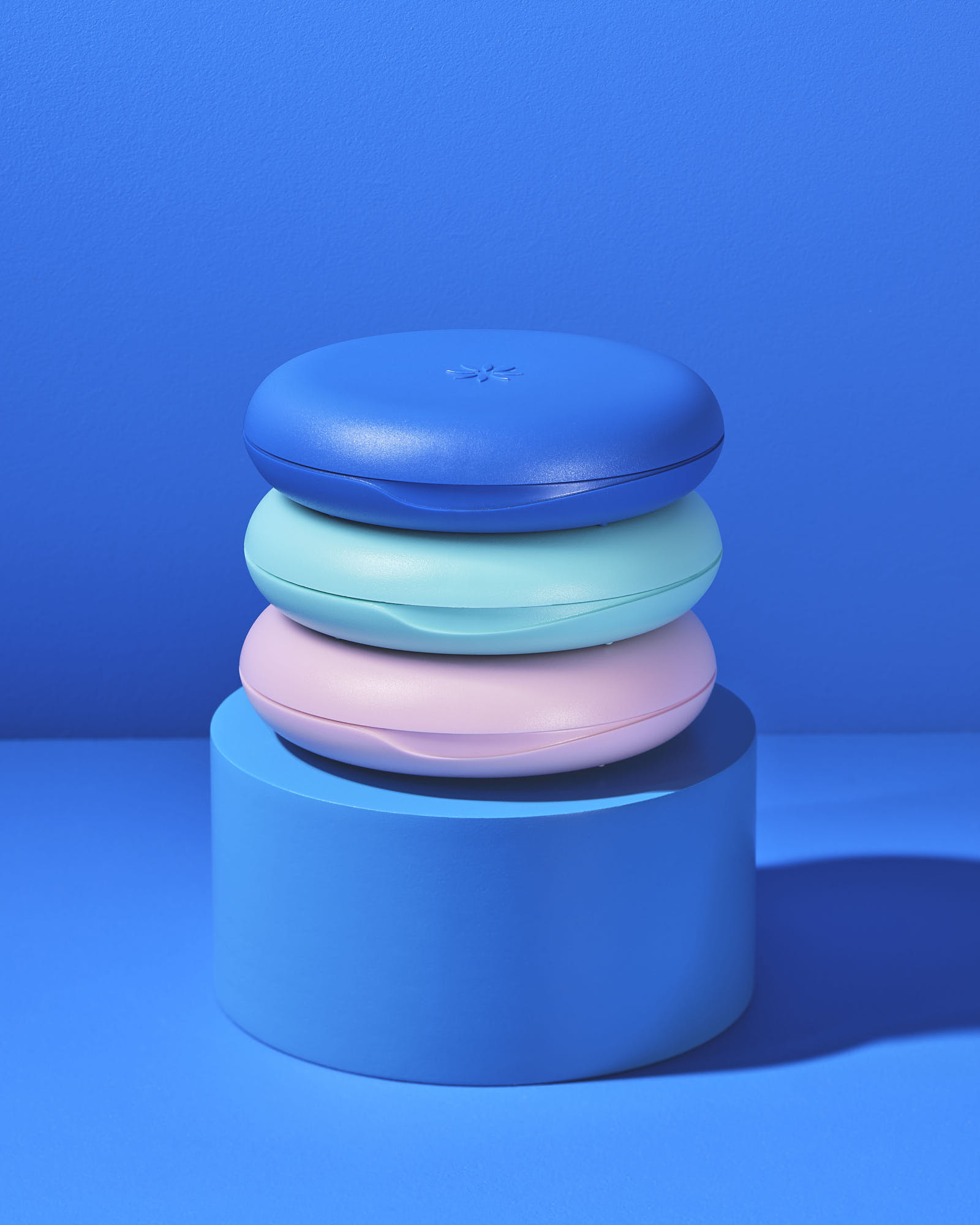 Colorful stack of round blue, mint, and pink cases on a blue pedestal.