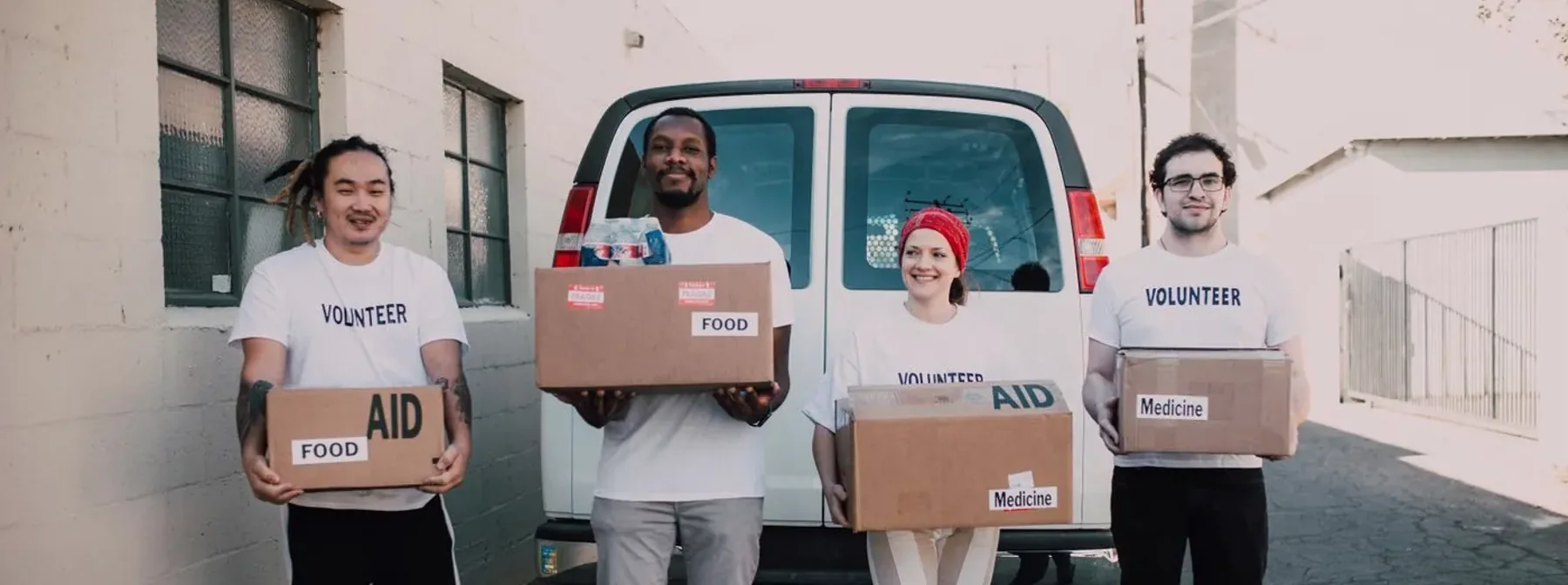 Volunteers holding boxes of donated food in front of a van