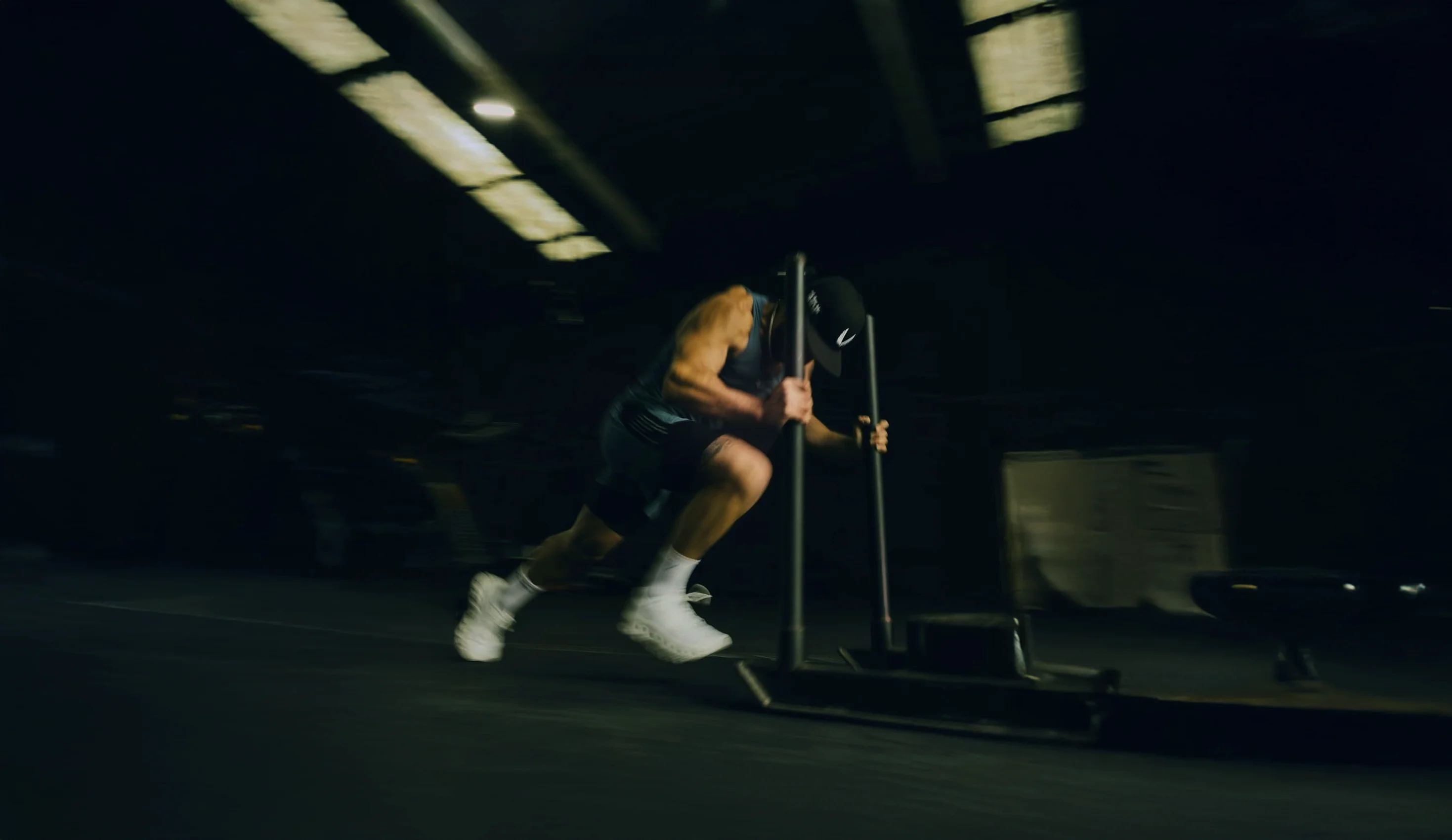 Man doing a sled push workout in a dimly lit gym.