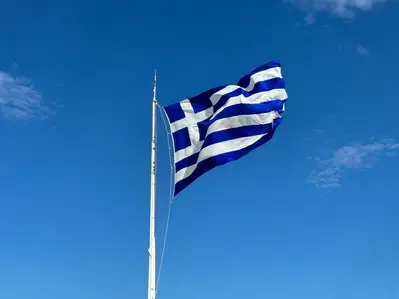 Greek flag waving on a flagpole against a clear blue sky