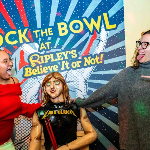 两位女性在一个标有“在信不信由你的瑞普利玩转保龄球！”的标牌前模仿着与模特一起吐舌头的姿势。