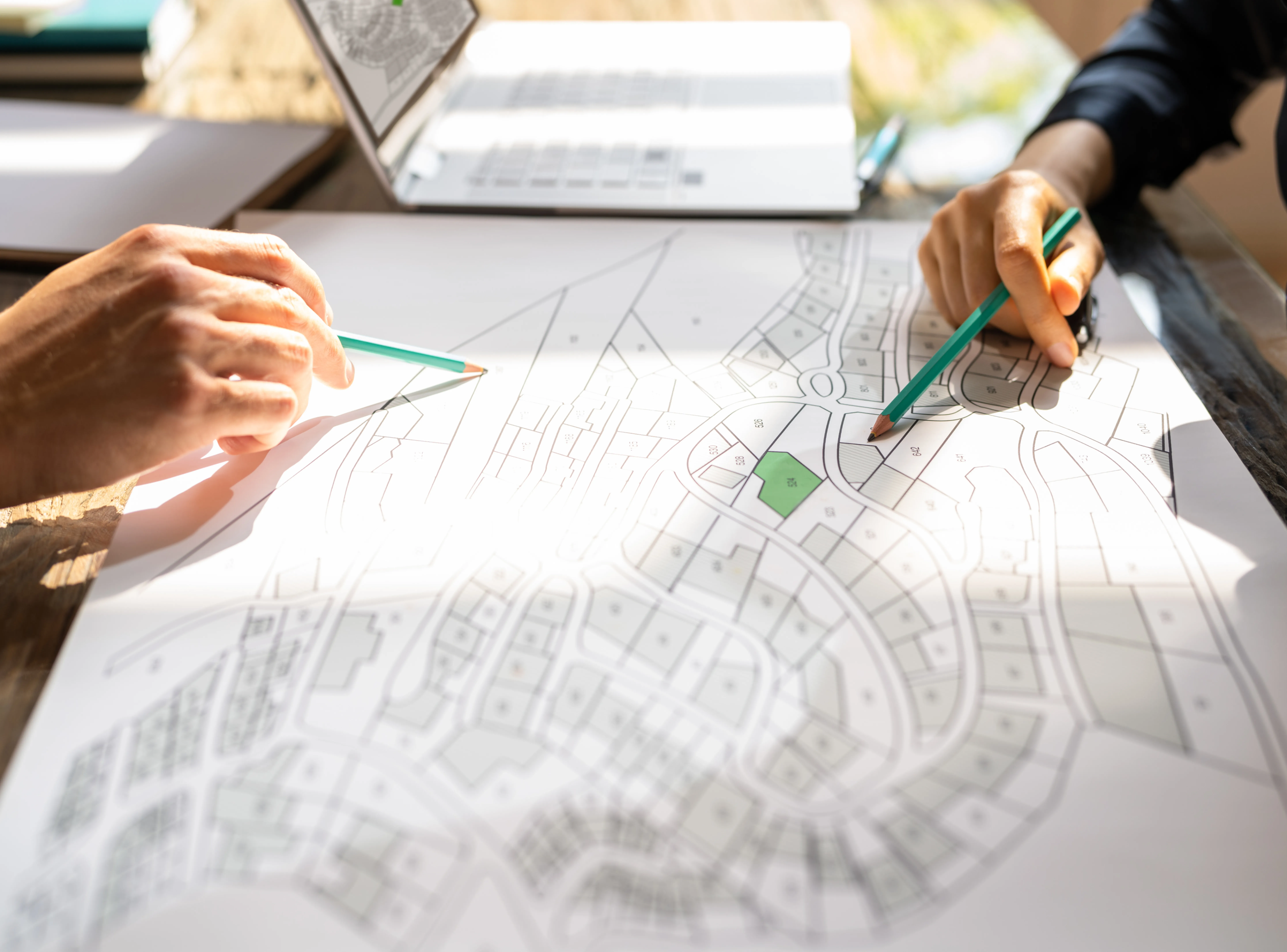 Close-up of architects using pencils to draft detailed technical site plans and urban layouts on large paper.