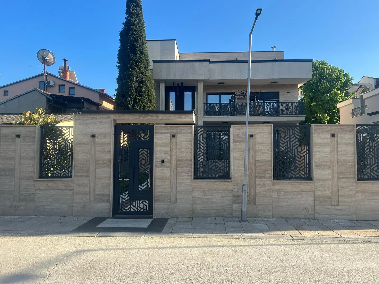 Street-facing view of a contemporary private residence in Skopje, featuring a stone façade, decorative metal fencing, and clean architectural lines. Designed and supervised by Terraplan Partners.