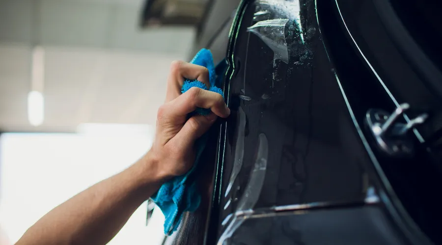 Hand cleaning black car door with microfiber cloth.
