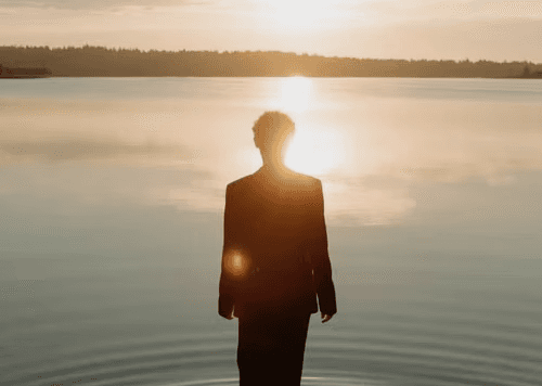 A silhouette of a hand seemingly touching the sun, which is setting over a body of water