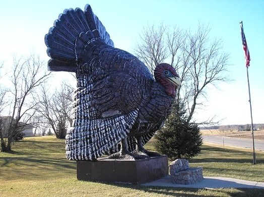 A sculpture or statue of a turkey put in a park near a stone bench.