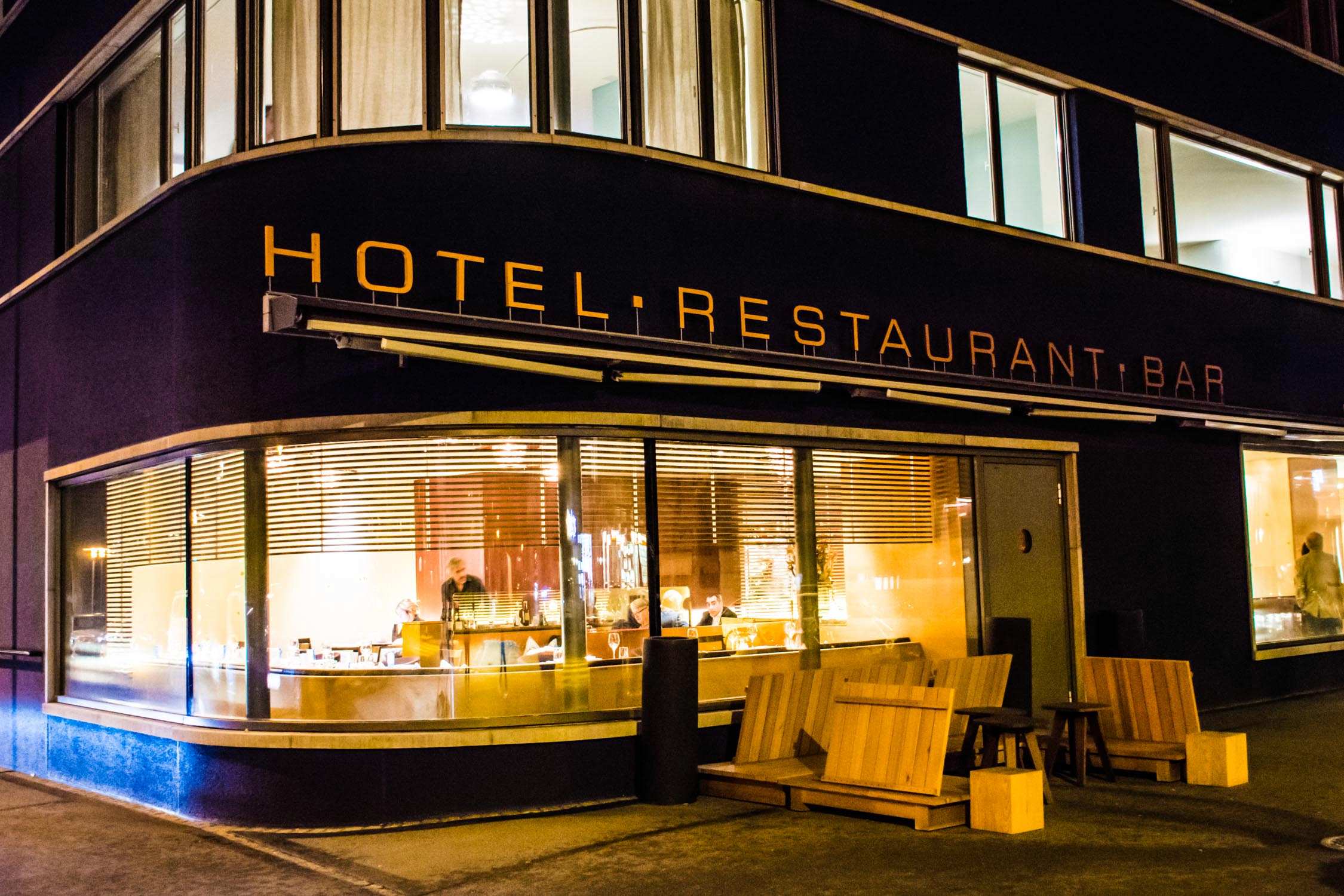 A modern hotel and restaurant building at night with illuminated windows and a large glass storefront.